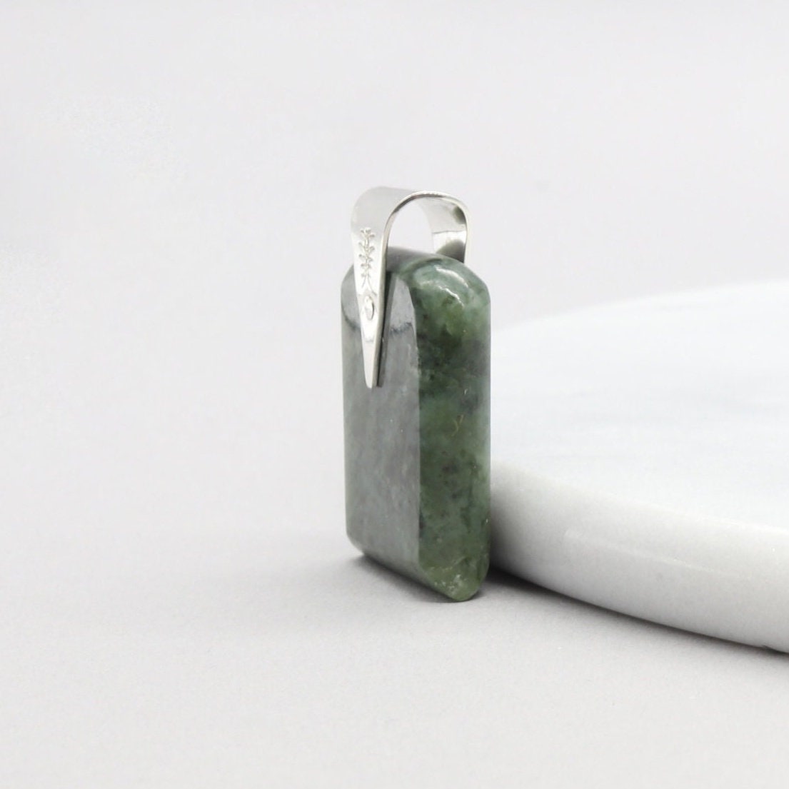 A Wyoming (Nephrite) Jade that I shaped and polished to bring out the light to dark sage translucent colors and patterns, into a distinctive tombstone tag shape. The custom-crafted bail with the Elkhorn Silver™ Crest makers mark, is sculpted from tarnish resistant and hypoallergenic sterling Argentium® 935 Silver.