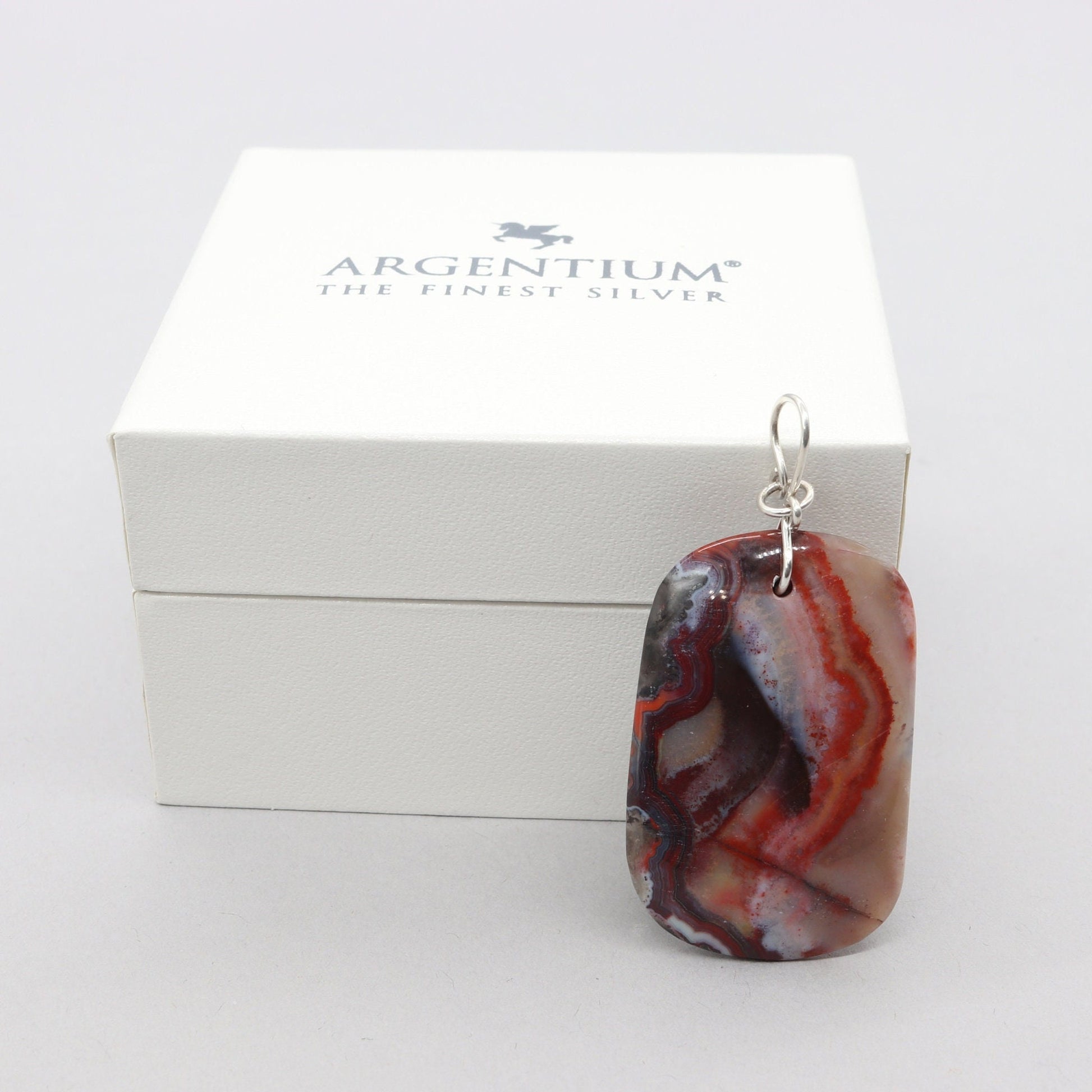 A 1.95 inch Red Mexico Agate hand-cut and freeform polished to bring out the mauve gray and deep red patterns and translucent colors. Crafted with an original infinity bow wire bail in Argentium 935 silver known for its higher silver content and its ability to resist tarnishing and keep on shining.  Ready to gift in a stylish gift box.