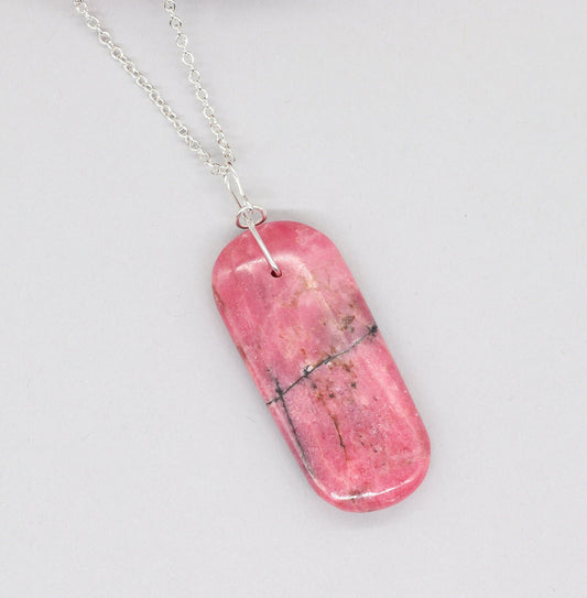 A natural Rhodonite crystal pendant in candy pink with black inclusions, sourced from our personal collection. This gemstone has been handcut and polished in our Missouri studio to highlight its natural beauty and crafted with an infinity shaped bow bail, in sterling Argentium 935 silver. To complete the look a complementary 935 Argentium silver chain is included.