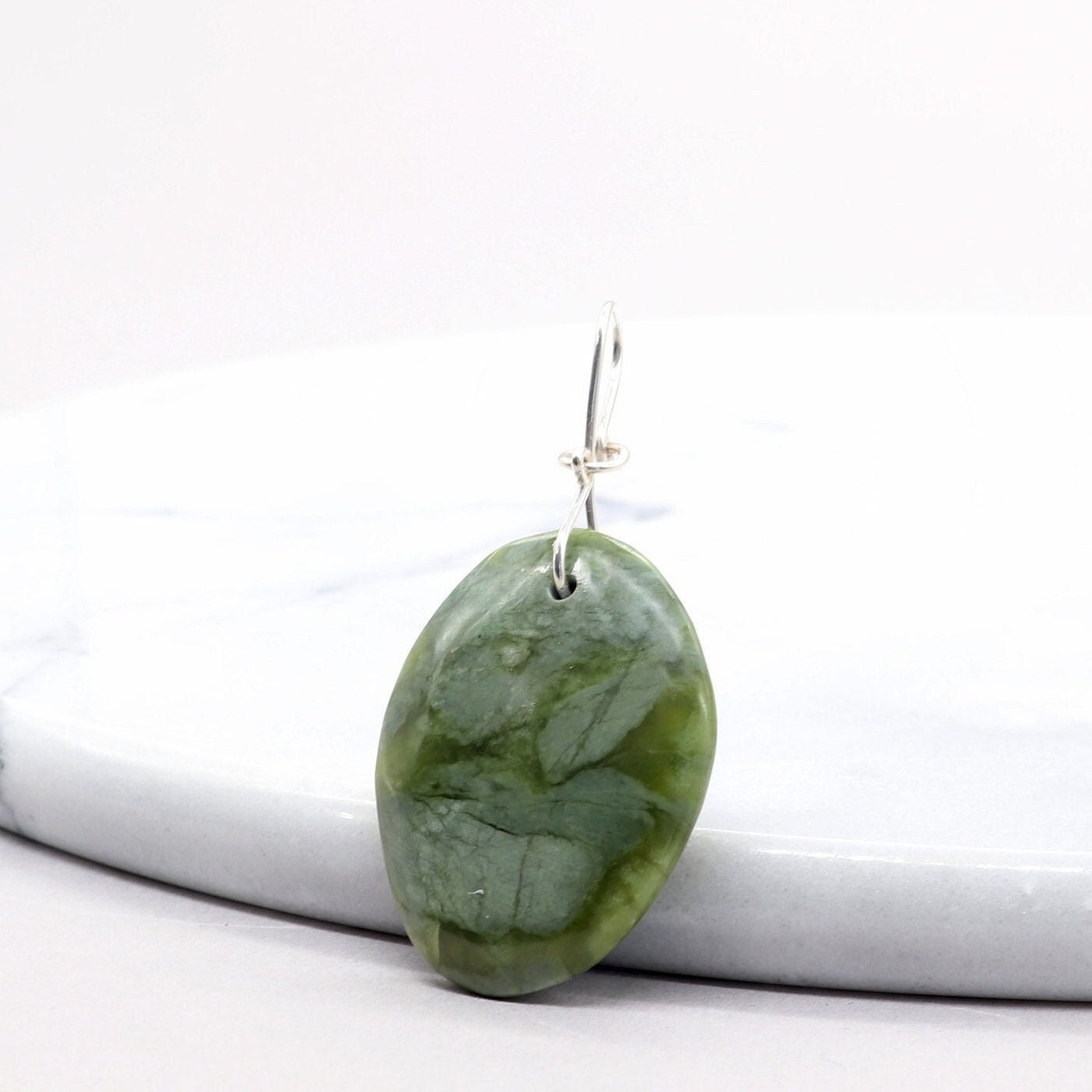 A California Jade gemstone pendant. Handcut and polished to showcase its unique translucent qualities, green hues and striking patterns on both sides. The pendant is designed with an original infinity bow shaped wire bail made from sterling Argentium® 935 Silver that is tarnish resistance and has a remarkable shine. The complete the look a complementary 935 Argentium silver chain is included.