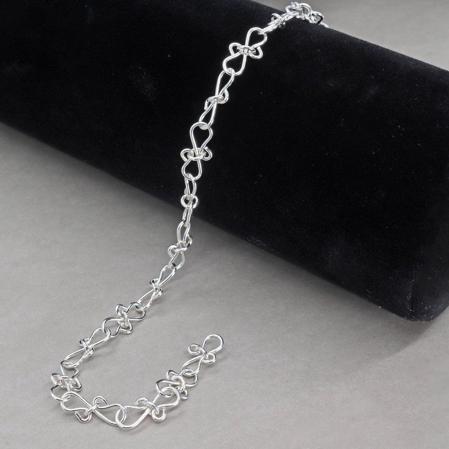 Infinity bow shaped chain bracelet handcrafted from solid sterling 935 Argentium Silver, ensuring its resistance to tarnish while being hypoallergenic for sensitive skin. The bracelet measures 7.5 in length, with an adjustable design that allows you to find the perfect fit by increments of half inch. A custom S hook clasp that enables easy wearing and removal.