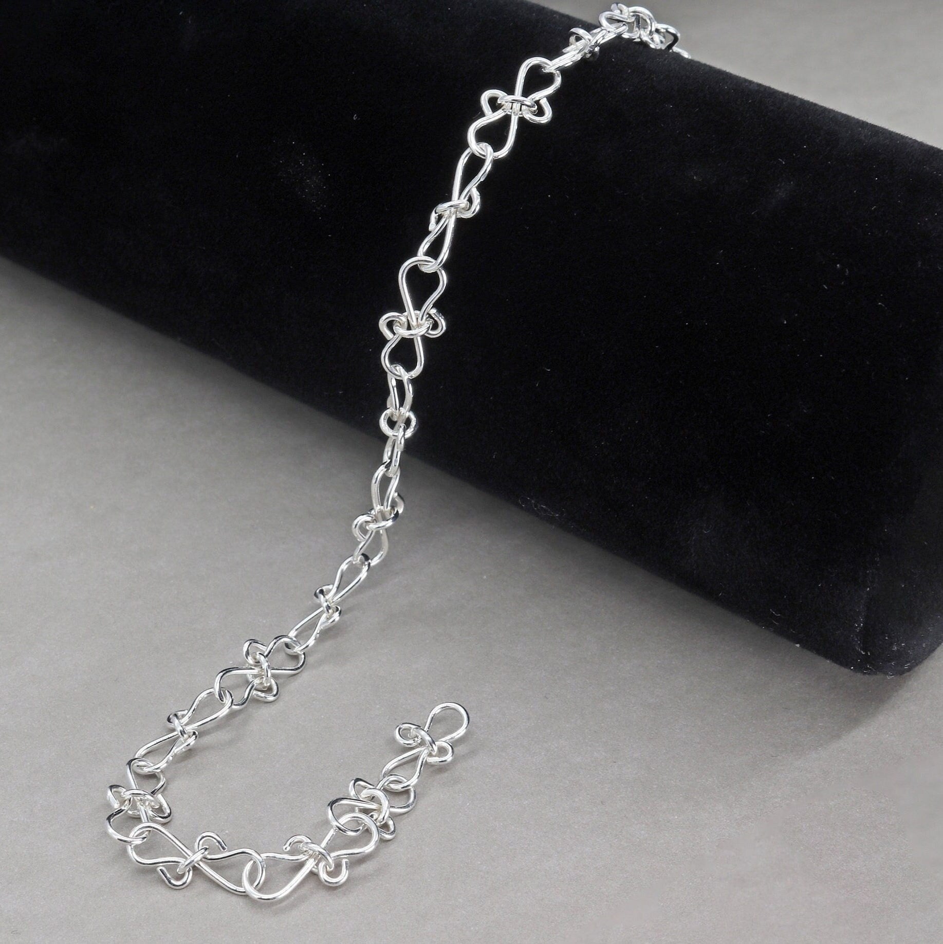 Infinity bow shaped chain bracelet handcrafted from solid sterling 935 Argentium Silver, ensuring its resistance to tarnish while being hypoallergenic for sensitive skin. The bracelet measures 7.5 in length, with an adjustable design that allows you to find the perfect fit by increments of half inch. A custom S hook clasp that enables easy wearing and removal.