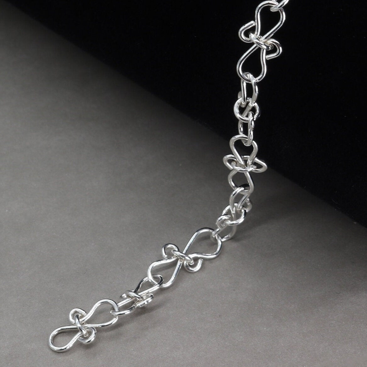 Infinity bow shaped chain bracelet handcrafted from solid sterling 935 Argentium Silver, ensuring its resistance to tarnish while being hypoallergenic for sensitive skin. The bracelet measures 7.5 in length, with an adjustable design that allows you to find the perfect fit by increments of half inch. A custom S hook clasp that enables easy wearing and removal.