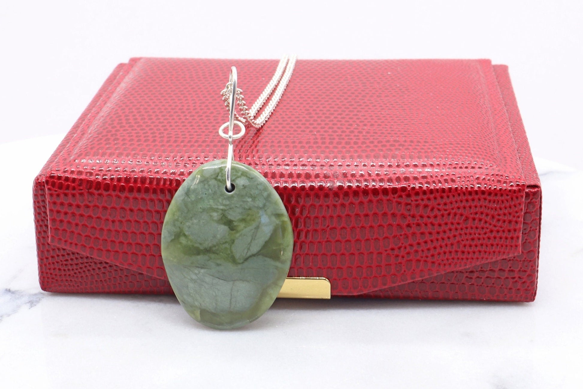 A California Jade gemstone pendant. Handcut and polished to showcase its unique translucent qualities, green hues and striking patterns on both sides. The pendant is designed with an original infinity bow shaped wire bail made from sterling Argentium® 935 Silver that is tarnish resistance and has a remarkable shine. The complete the look a complementary 935 Argentium silver chain is included.  Ready to gift in a red faux leather box.