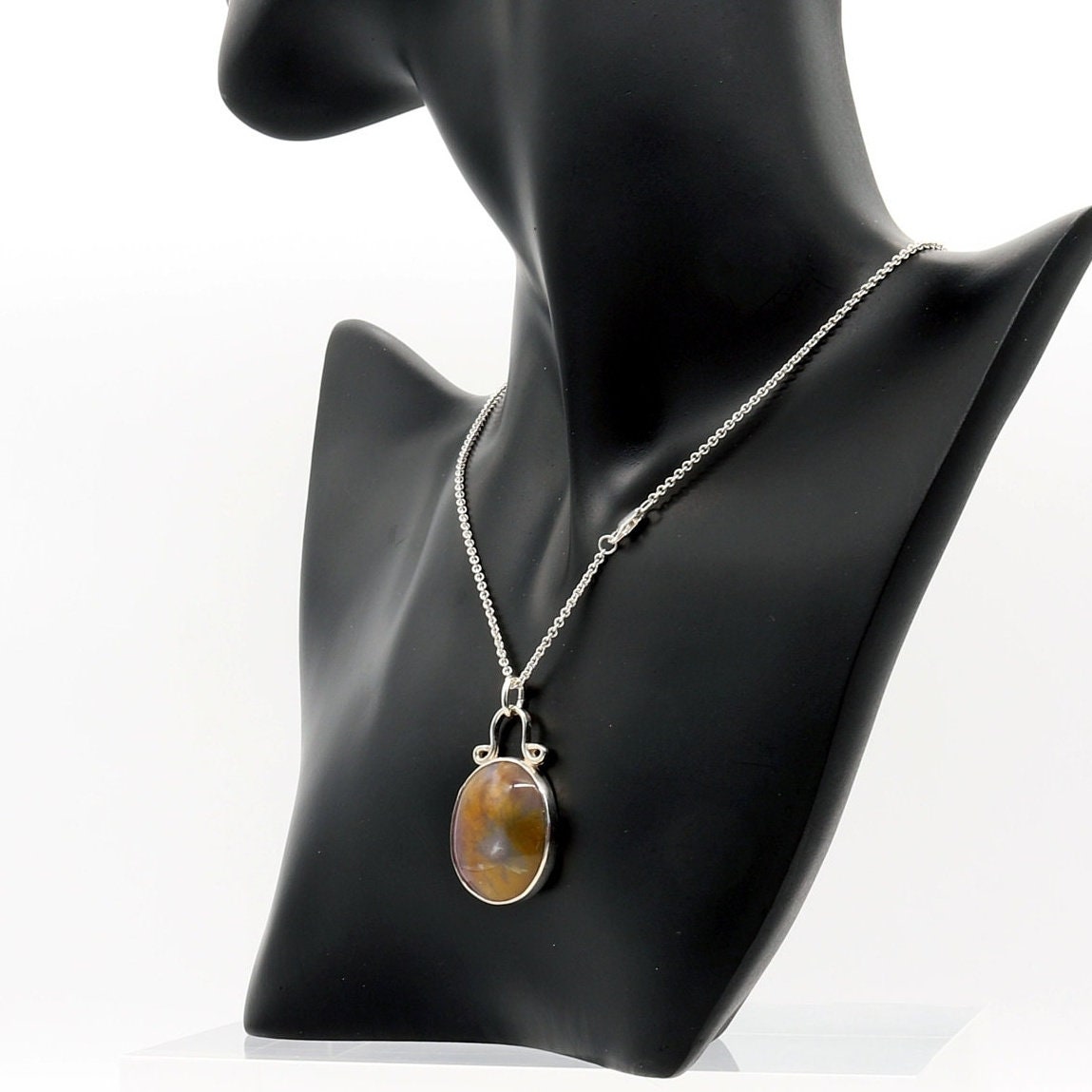 A Petrified Rainbow Wood stone found in Arizona's Petrified Forest, carefully polished by hand in our studio to reveal gold, gray and deep red hues showcased in a vintage style setting. Hanging from a unique and elegant sterling 935 Argentium Silver bail and setting, this piece is sure to capture your attention and become a cherished part of your jewelry collection. To complete the look is a complementary 1.7 sterling 935 Argentium silver necklace chain with lobster clasp.