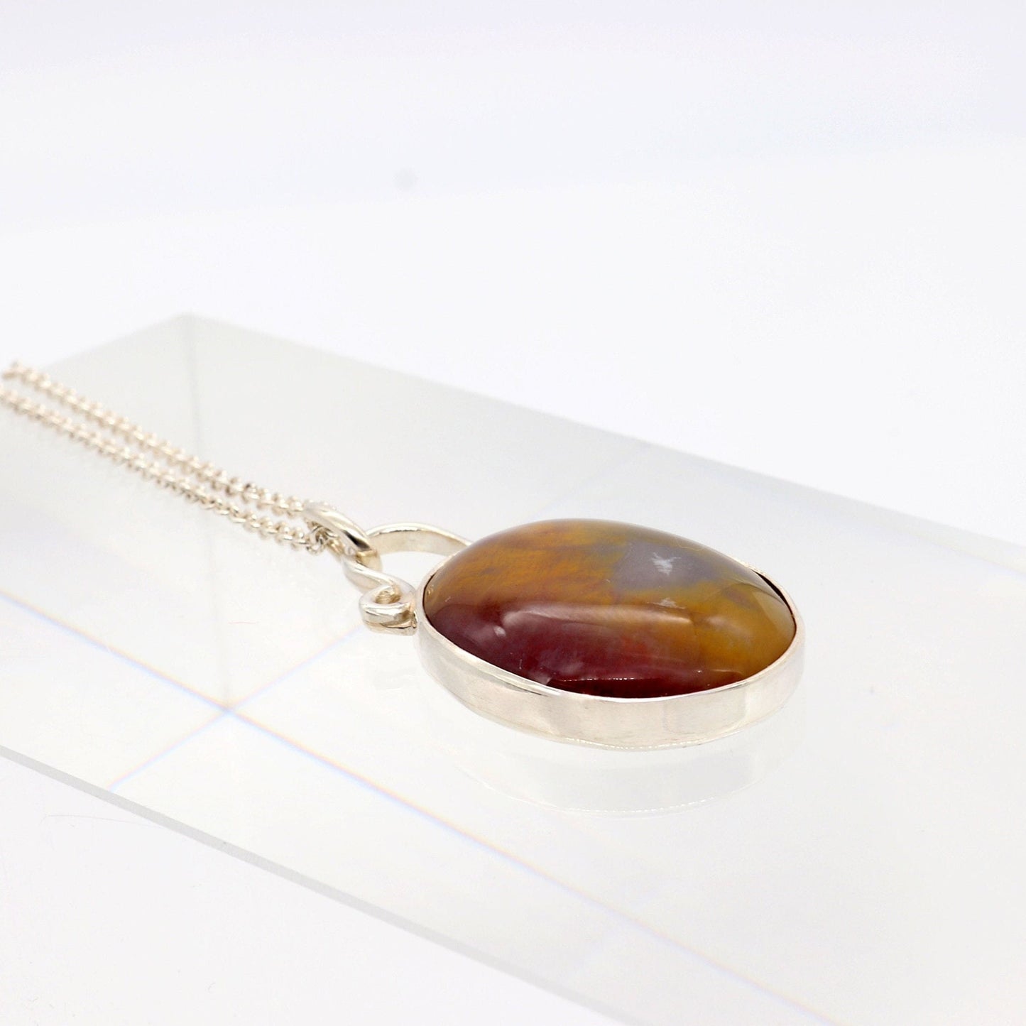 A Petrified Rainbow Wood stone found in Arizona's Petrified Forest, carefully polished by hand in our studio to reveal gold, gray and deep red hues showcased in a vintage style setting. Hanging from a unique and elegant sterling 935 Argentium Silver bail and setting, this piece is sure to capture your attention and become a cherished part of your jewelry collection. To complete the look is a complementary 1.7 sterling 935 Argentium silver necklace chain with lobster clasp.
