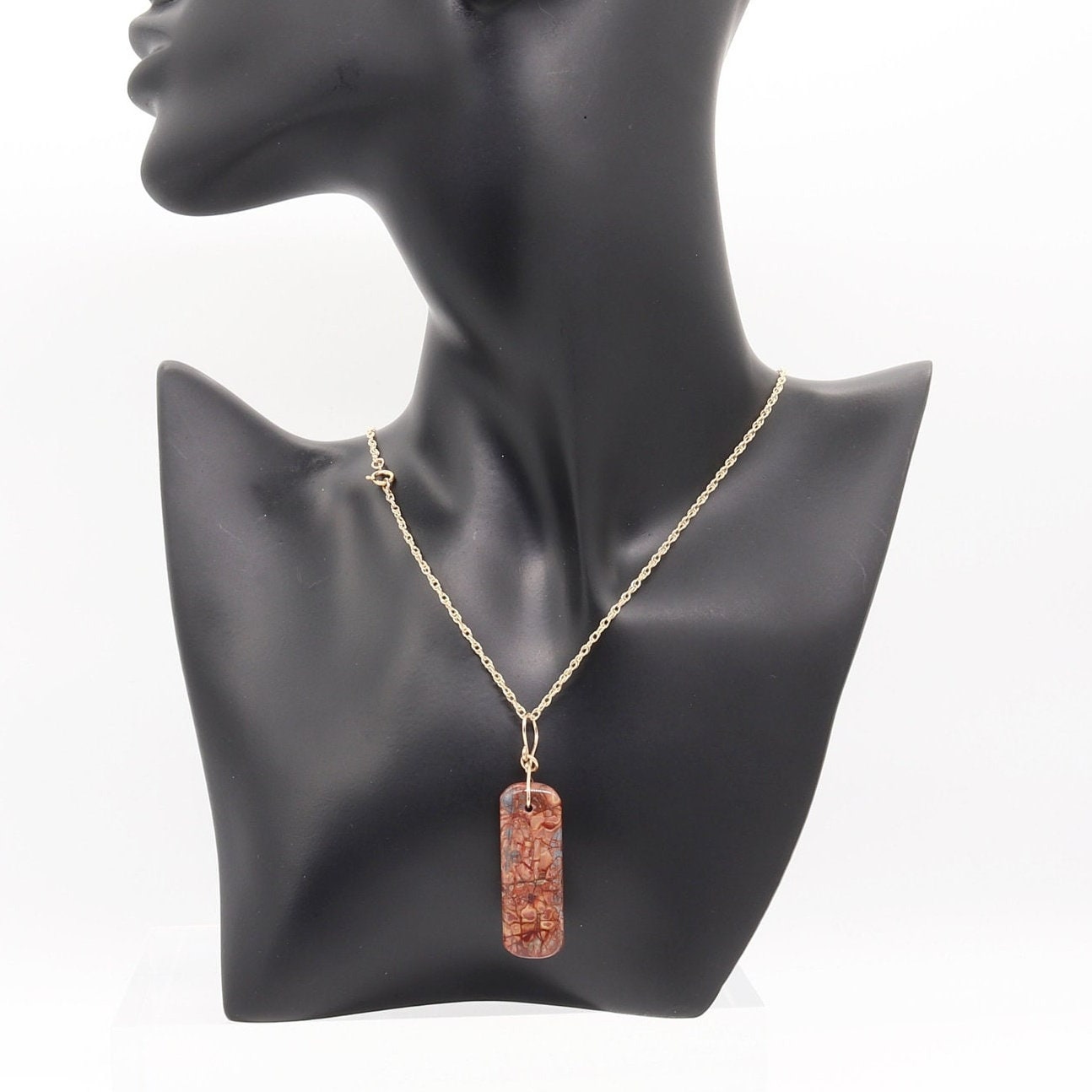 A beautiful natural 2.12 inch Stony Creek Jasper handcut and freeform polished to showcase the stunning red and blue patterns of the stone.
The custom 14/20 Yellow Gold-Filled wire infinity bow-shaped bail and the complementary double-rope necklace in 14/20 Yellow Gold-Filled completes the look. Versatile and stylish, this piece is perfect for any occasion.