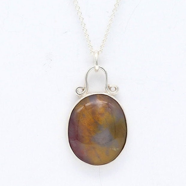 A Petrified Rainbow Wood stone found in Arizona's Petrified Forest, carefully polished by hand in our studio to reveal gold, gray and deep red hues showcased in a vintage style setting. Hanging from a unique and elegant sterling 935 Argentium Silver bail and setting, this piece is sure to capture your attention and become a cherished part of your jewelry collection. To complete the look is a complementary 1.7 sterling 935 Argentium silver necklace chain with lobster clasp.