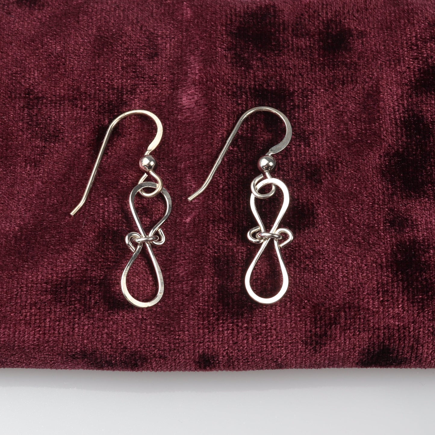 A pair of Silver Bow Earrings in solid premium 935 Argentium silver,with a hammered finish shown against burgundy velvet