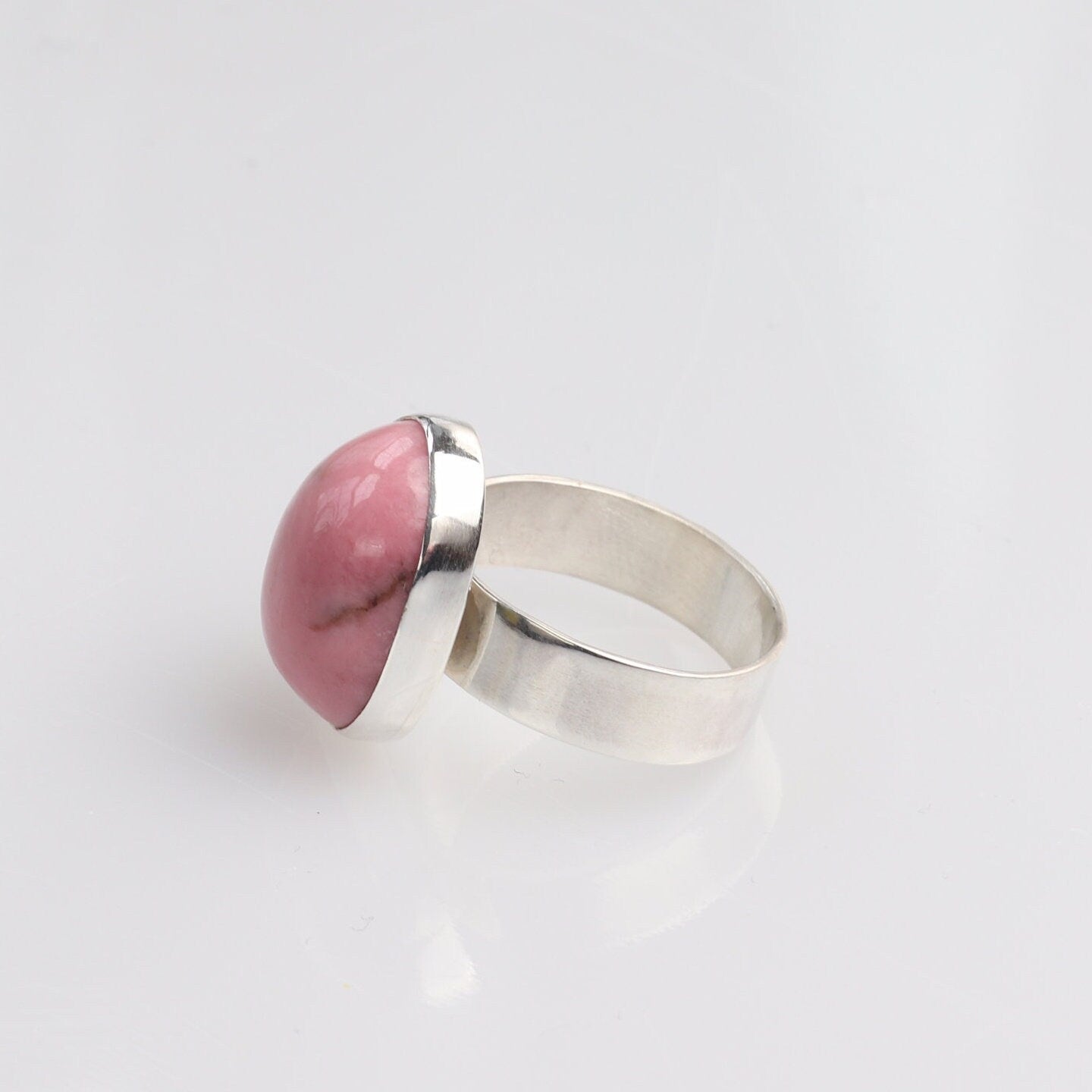 Left side of this handcrafted pink Rhodonite gemstone ring. The stone has been handcut and polished into a smooth cabochon to reveal its rich rose hue and subtle black veining.