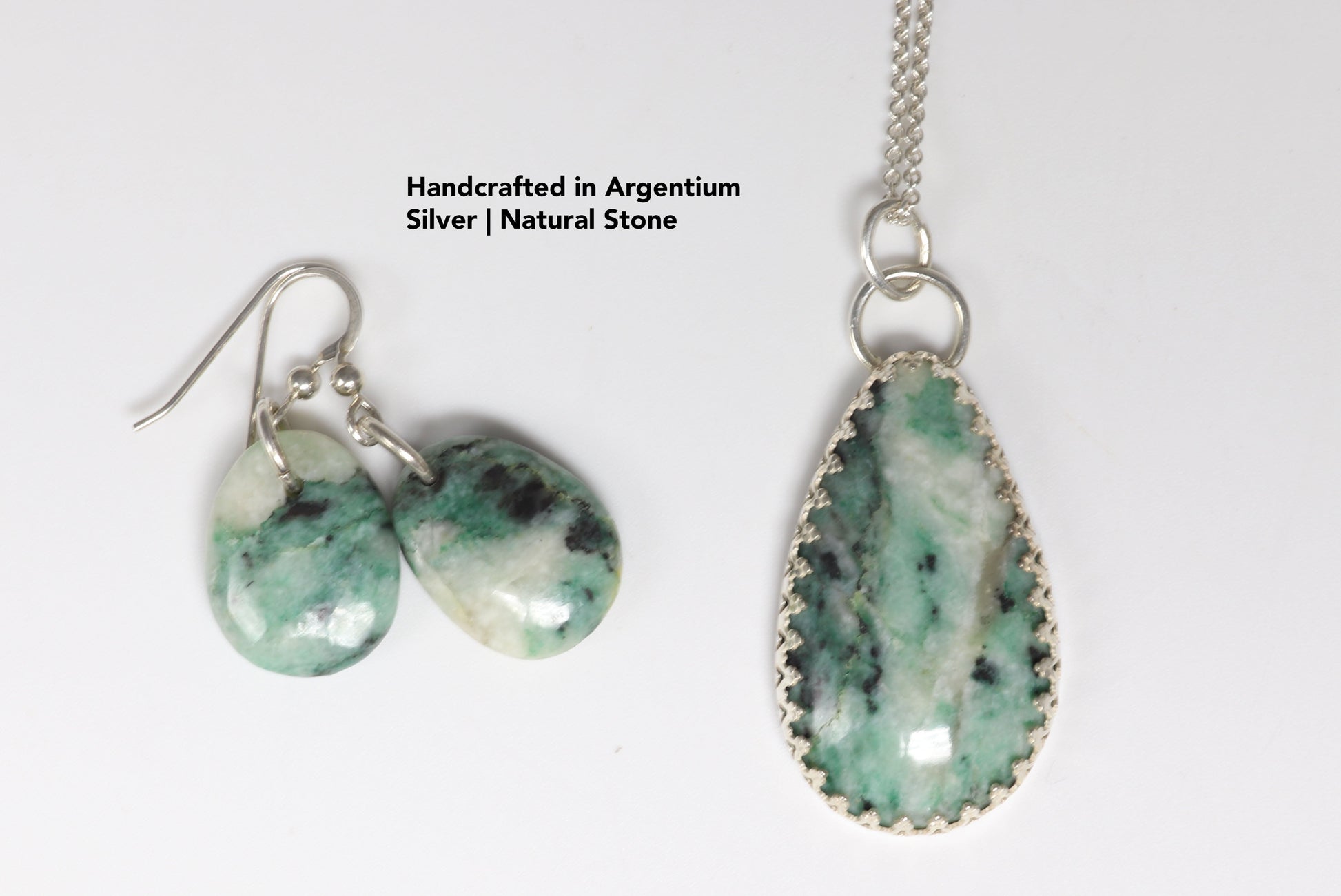A closeup of  the African Turquoise Jasper pendant is set including pendant and earrings in solid Argentium® 935 silver with a custom bezel, beautifully accented by a gallery-style border of inverted hearts.  The jewelry is set on white  background.