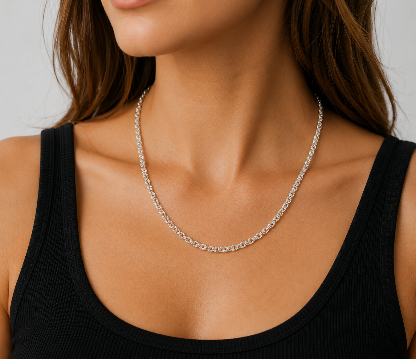 Silver necklace on a person wearing a black tank top against a neutral background