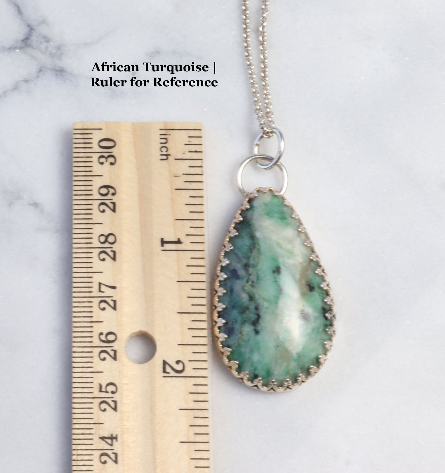 Ruler for reference next to 2.12inch pendant African Turquoise with green white and black natural patterns against a white marble background.