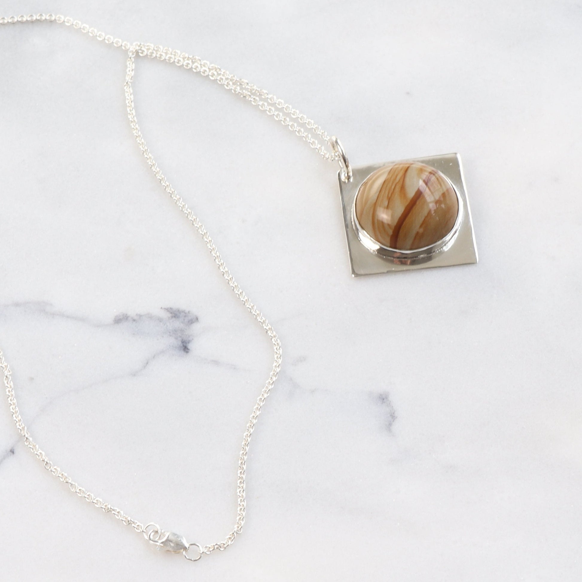A 1.625 inch hand-cut and polished one-of-a-kind Picture Jasper cabochon with a beautiful landscape pattern and color bands set in a unique four-point diamond-shaped of sterling Argentium® 935 Silver paired with a complementary sterling Argentium 935 chain.