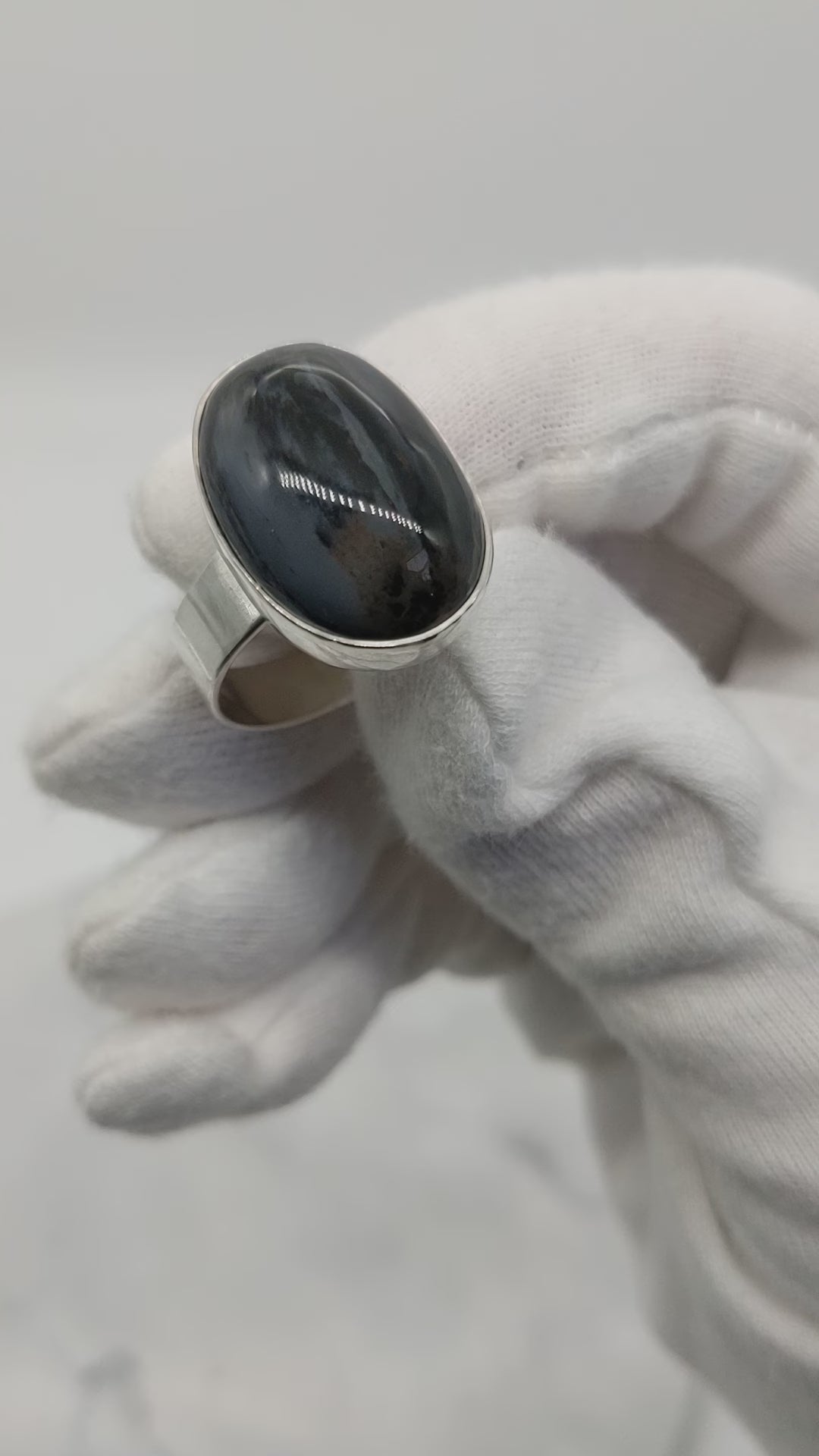 Close-up demo of polished black and blue Petrified Wood cabochon in fine silver bezel