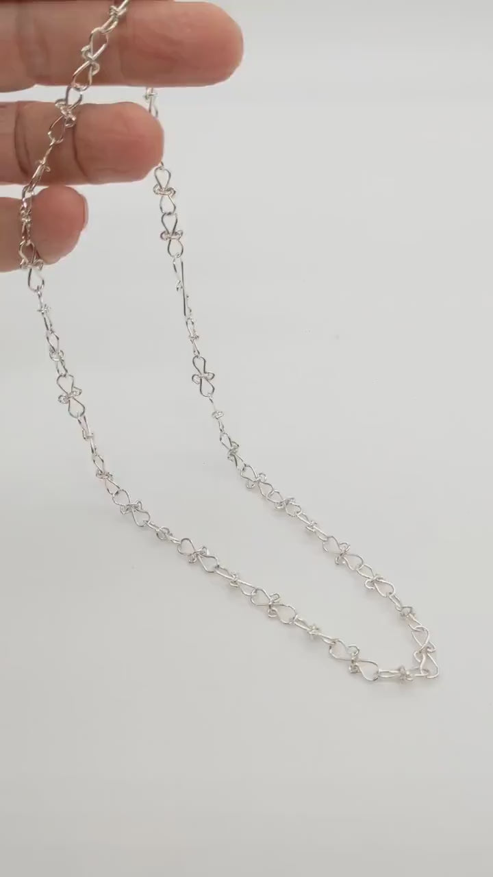 Hand demonstration of the figure 8 infinity bow necklace.   Showing the features and shine of the necklace.