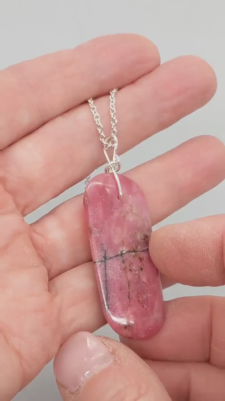 Video showing pink Rhodonite pendant being rotated by hand to display front and back sides, highlighting custom 935 Argentium® silver bail.