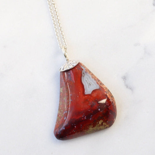 A 1.81 inch Red Jasper Agate Pendant, handcrafted in our small town Missouri studio. Handcut and freeform polished on both sides, showcasing the captivating patterns and rich red hues of this reversible piece. The custom crafted bail in sterling 935 Argentium Silver adds a touch of elegance. To make this piece ready to wear, a matching 1.7 Argentium silver chain is optional with gift box. This pendant could be used as a focal piece for your next beading project.