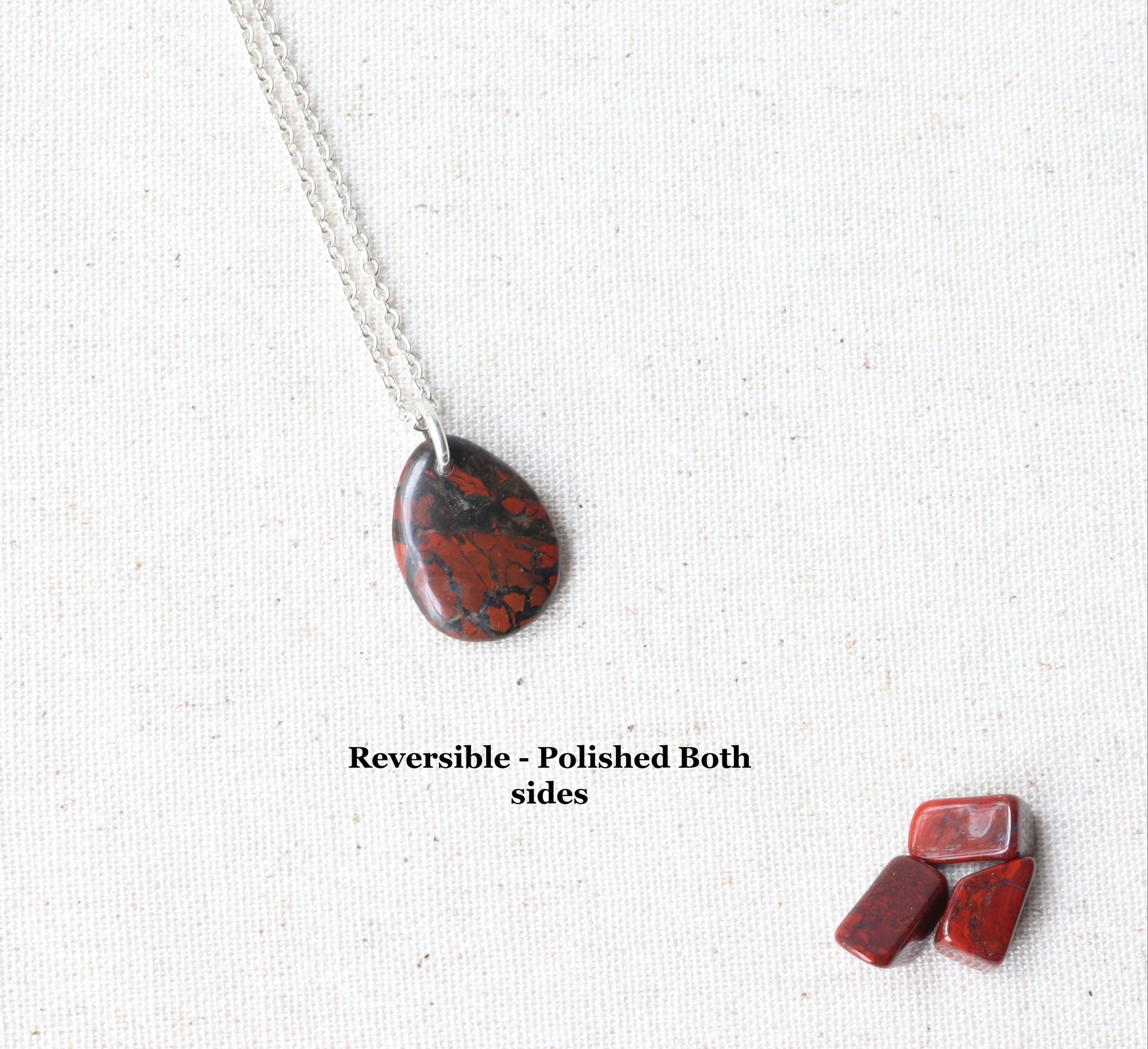Red Jasper Pendant shown with optional chain.  Polished on both sides provides a reversible versatile piece.  Chips of red jasper shown as props.