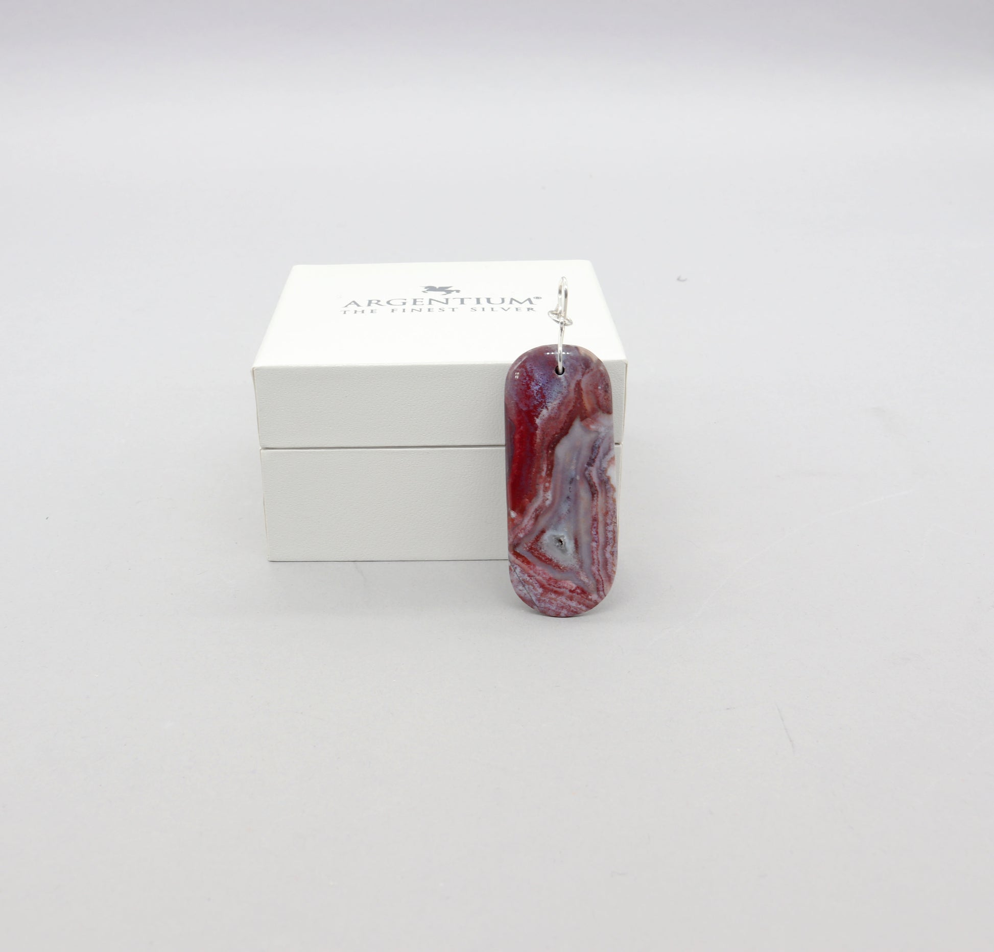 Handcrafted Red Mexico Agate pendant with mauve-gray and lavender hues, set in Argentium® 935 silver with a bow-shaped bail, presented in a white box labeled ‘ARGENTIUM – THE FINEST SILVER’.