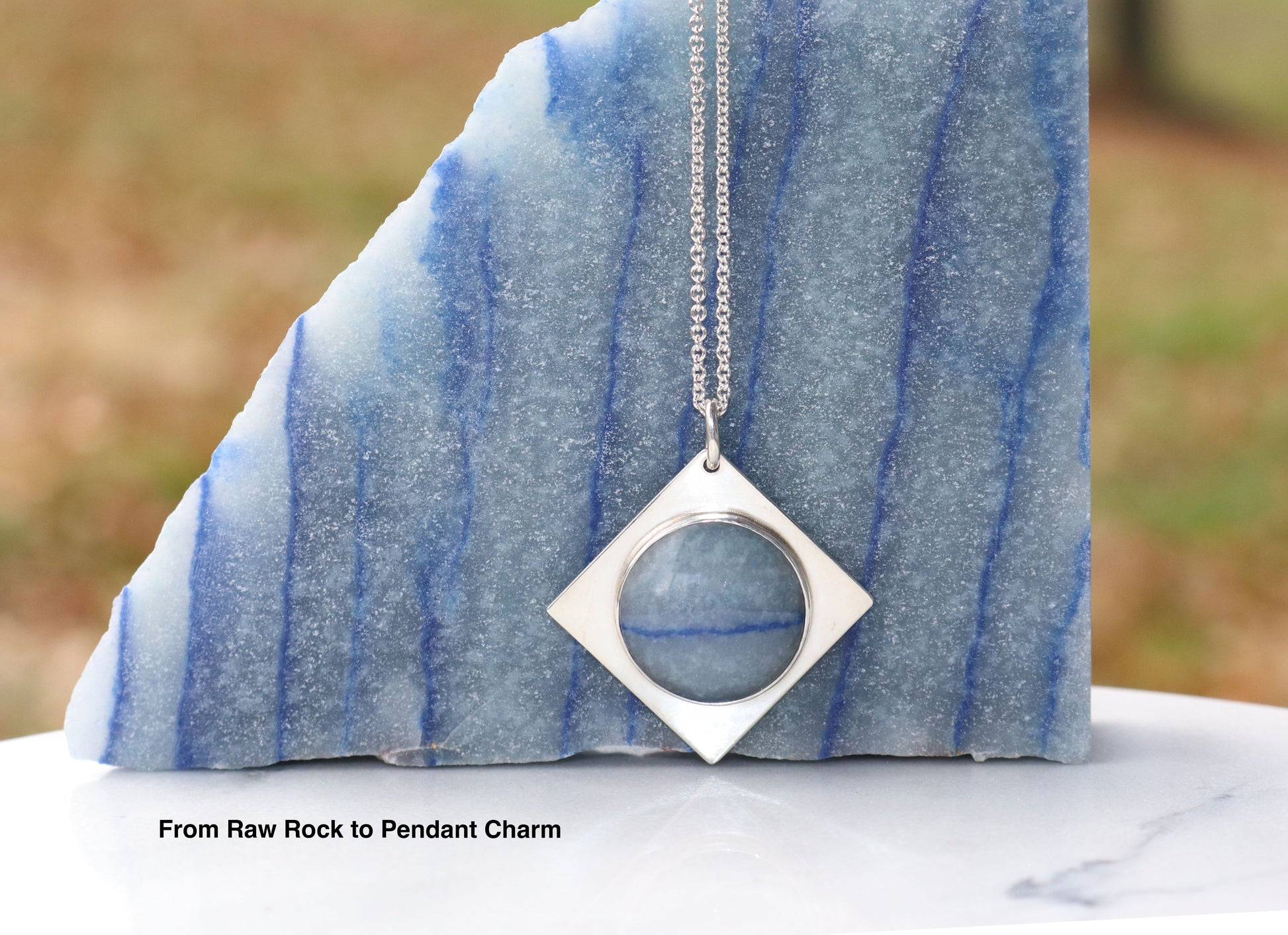 A Celestial Blue Aventurine pendant with Saturn-like inclusions. Handcut and set in 935 Argentium® Silver. Includes 18” chain. Gift-ready and unique.  Shown next to the same rock the pendant was crafted from against and outdoor setting.