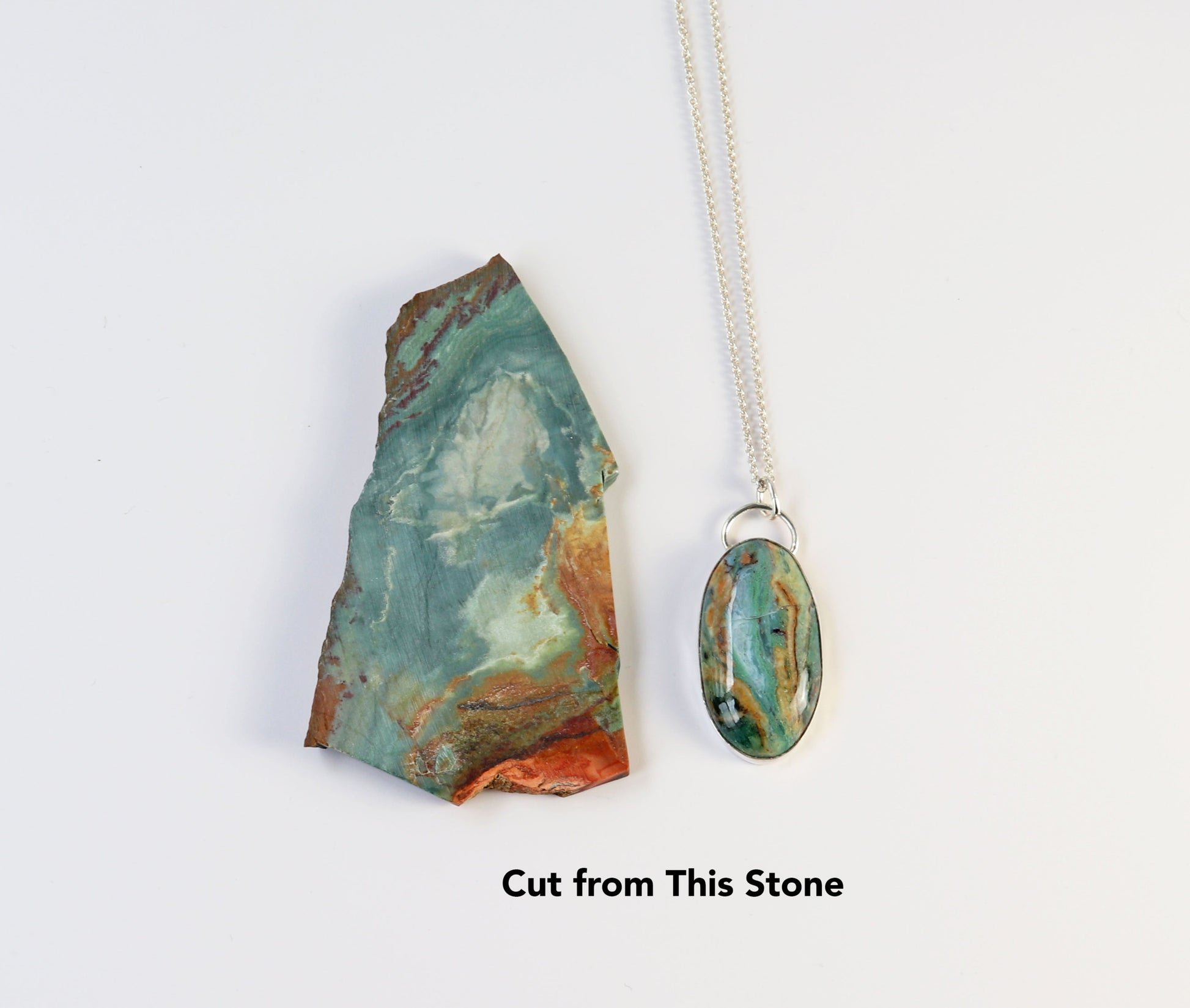 Flat lay of a handcrafted Sonoran Jasper pendant and the original slab it was cut from. Both feature teal and earthy brown tones. Pendant set in 935 Argentium® Silver with chain shown.