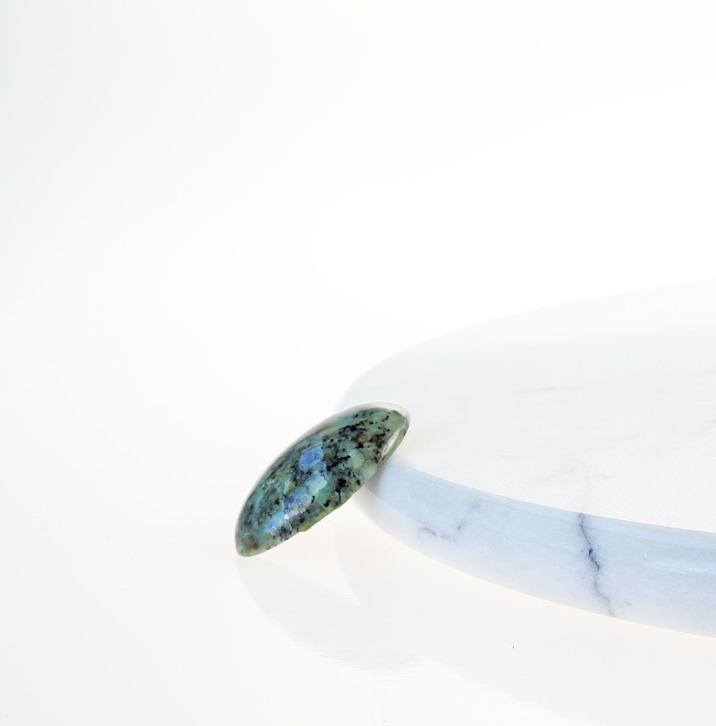 A Fraser River Turquoise gemstone with blue-green hues contrasted with a bold black matrix gemstone on a white background
