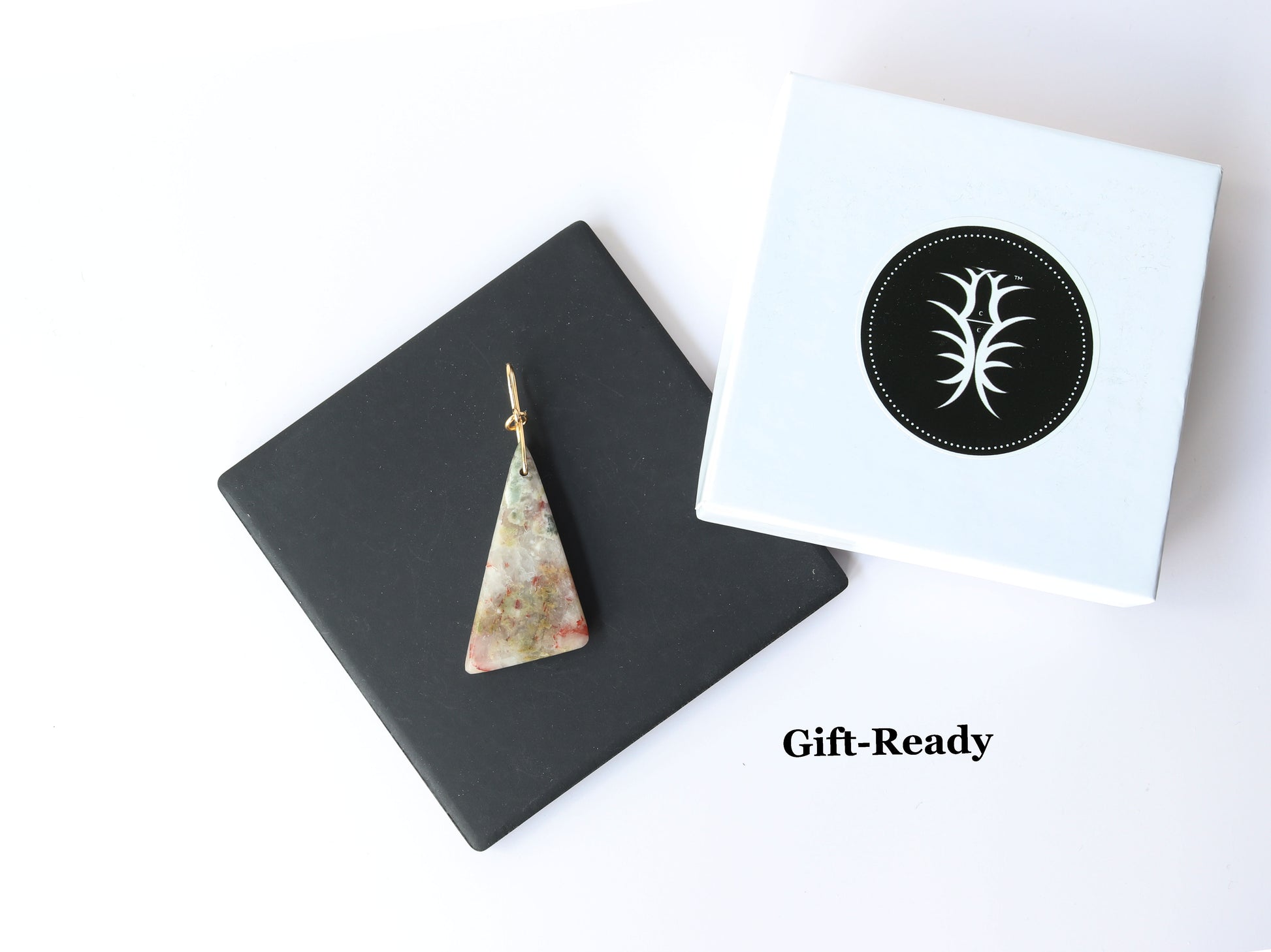 A Sunstone Pendant hand cut and polished on both sides to showcase the unique  blend of earthy reds, muted greens, and translucent swirls of gray and creamy white of earthy elegance.  This one-of-a-kind irregular triangle shape adds bold character to wire-wrapped jewelry, mixed-media designs, or statement necklaces.  Shown with signature gift box.