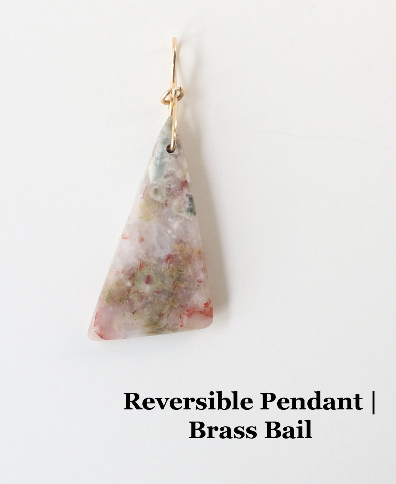 A Sunstone Pendant hand cut and polished on both sides to showcase the unique  blend of earthy reds, muted greens, and translucent swirls of gray and creamy white of earthy elegance.  This one-of-a-kind irregular triangle shape adds bold character to wire-wrapped jewelry, mixed-media designs, or statement necklaces.  Shown reverse or back-side against white background.