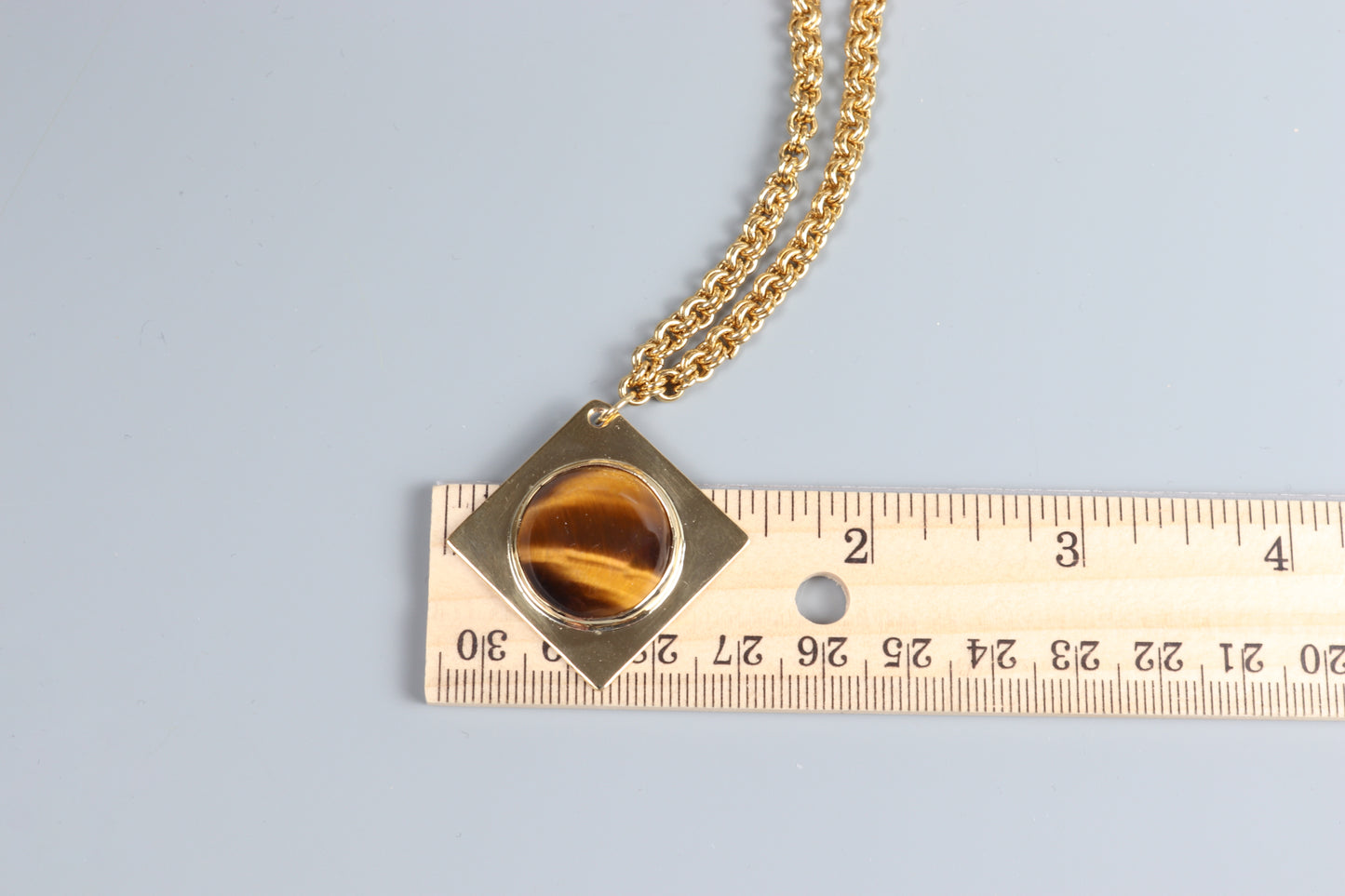 A closeup of a 1.625 Tiger’s Eye pendant, featuring a .75” round cabochon shown next to ruler for scale.