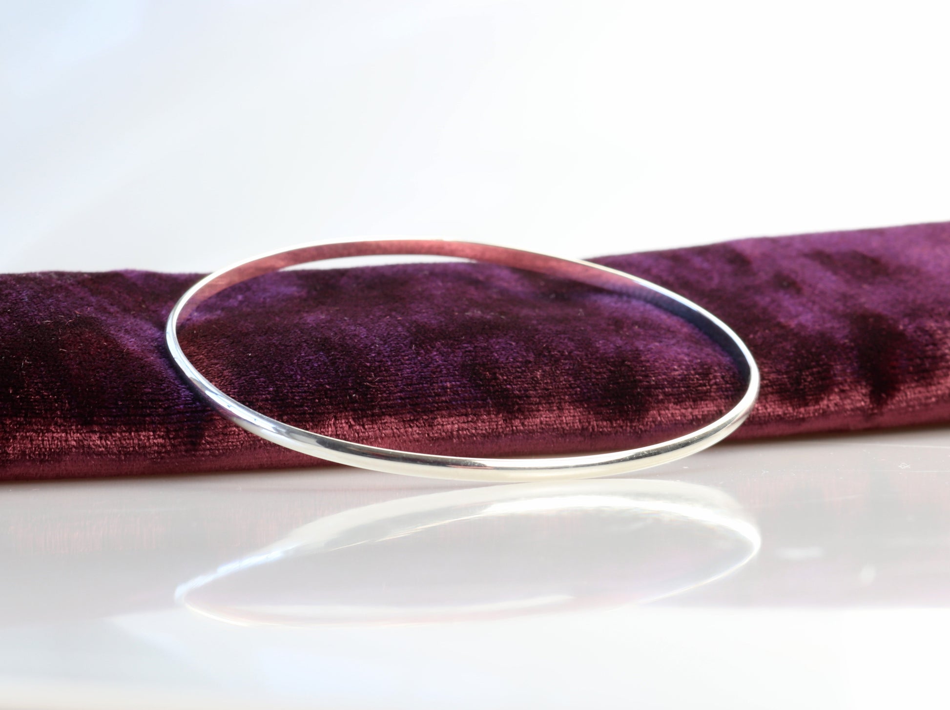 Bangle Bracelet shown leaning on burgundy velvet against a white background.