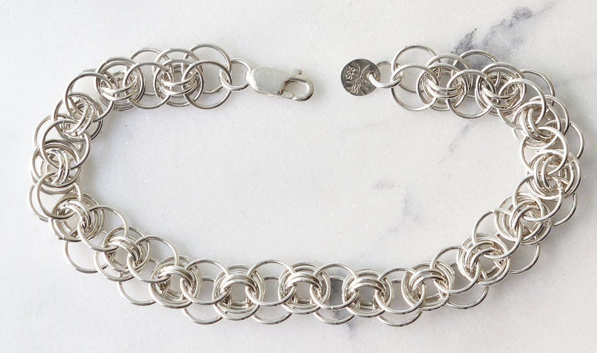 An Argentium silver helm chainmail bracelet with interlocking circular links and lobster clasp closure, displayed on a white marble surface.
