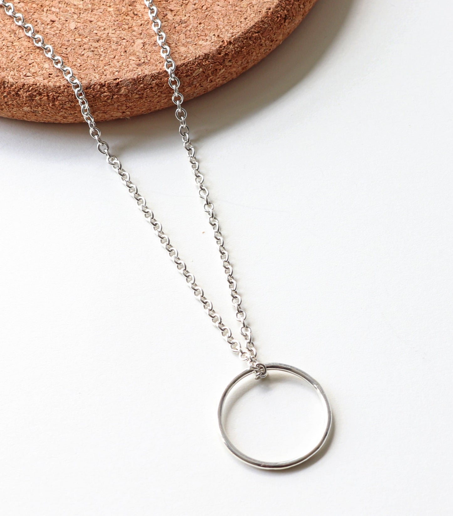 Argentium Silver open circle necklace on a white background with cork base. 