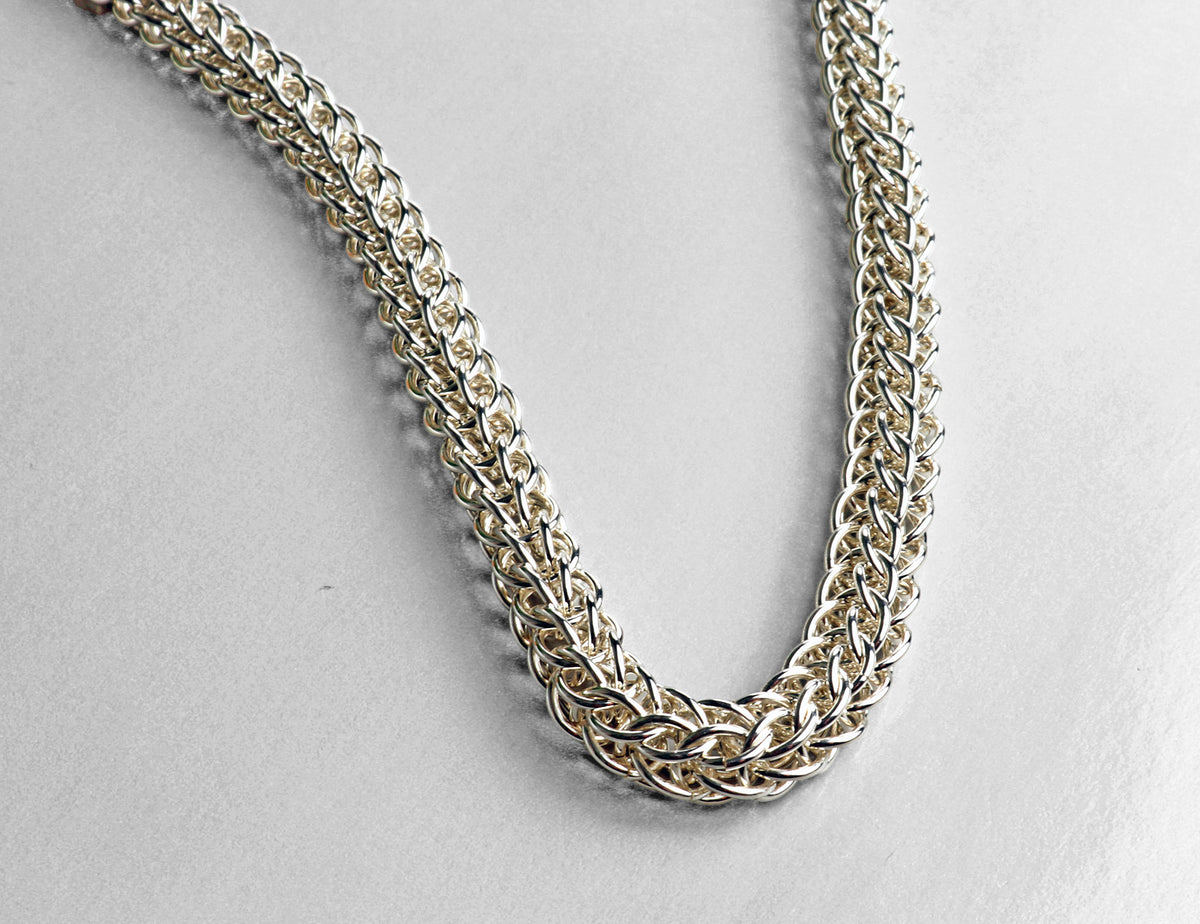 A close-up of an Argentium silver chain necklace with a full persian weave design, photographed on a plain light gray background.