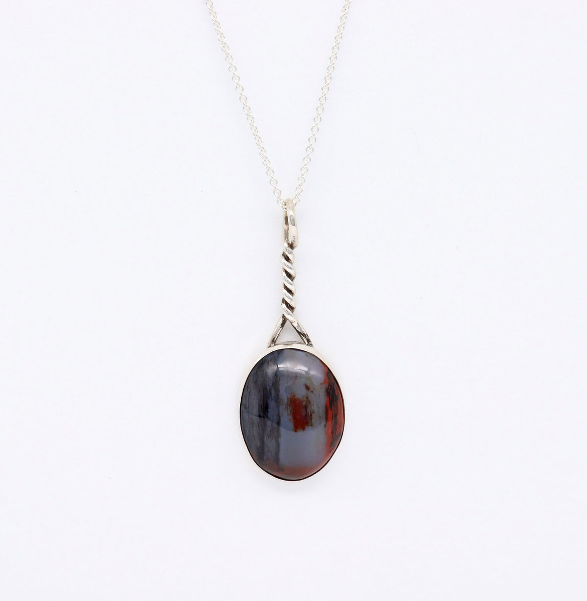An Argentium silver necklace with a twisted bail and an oval pendant featuring a dark, marbled pattern of black, gray, and reddish-brown of natural Petrified Rainbow Wood from Arizona, shown against a plain white background.