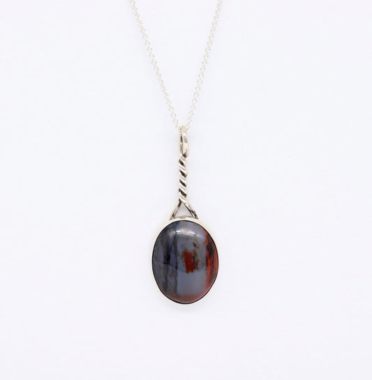 An Argentium silver necklace with a twisted bail and an oval pendant featuring a dark, marbled pattern of black, gray, and reddish-brown of natural Petrified Rainbow Wood from Arizona, shown against a plain white background.