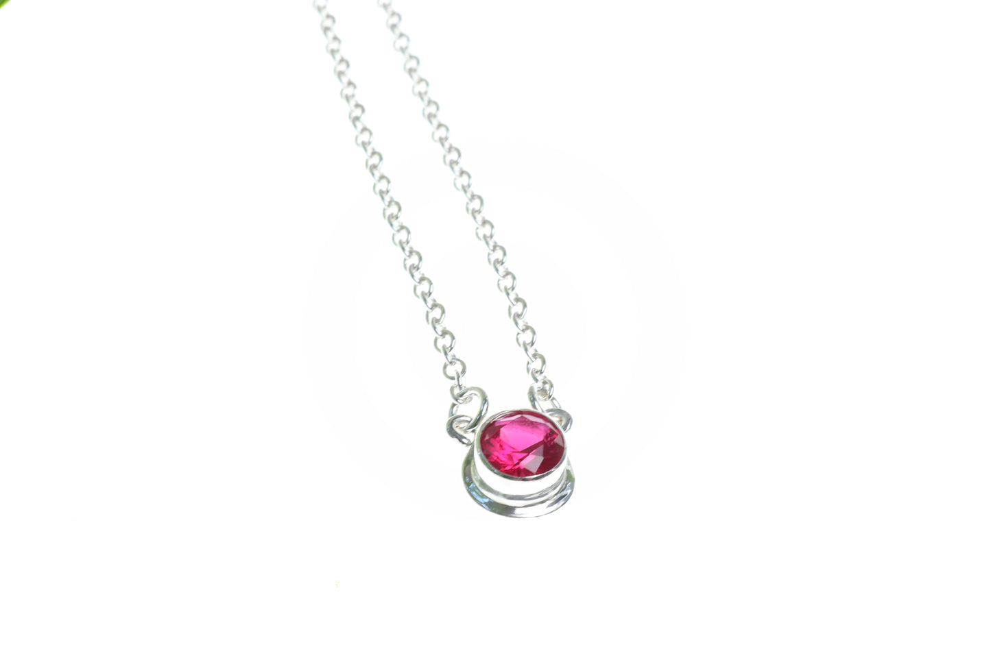 Closeup of ruby 6mm pendant necklace on white background.