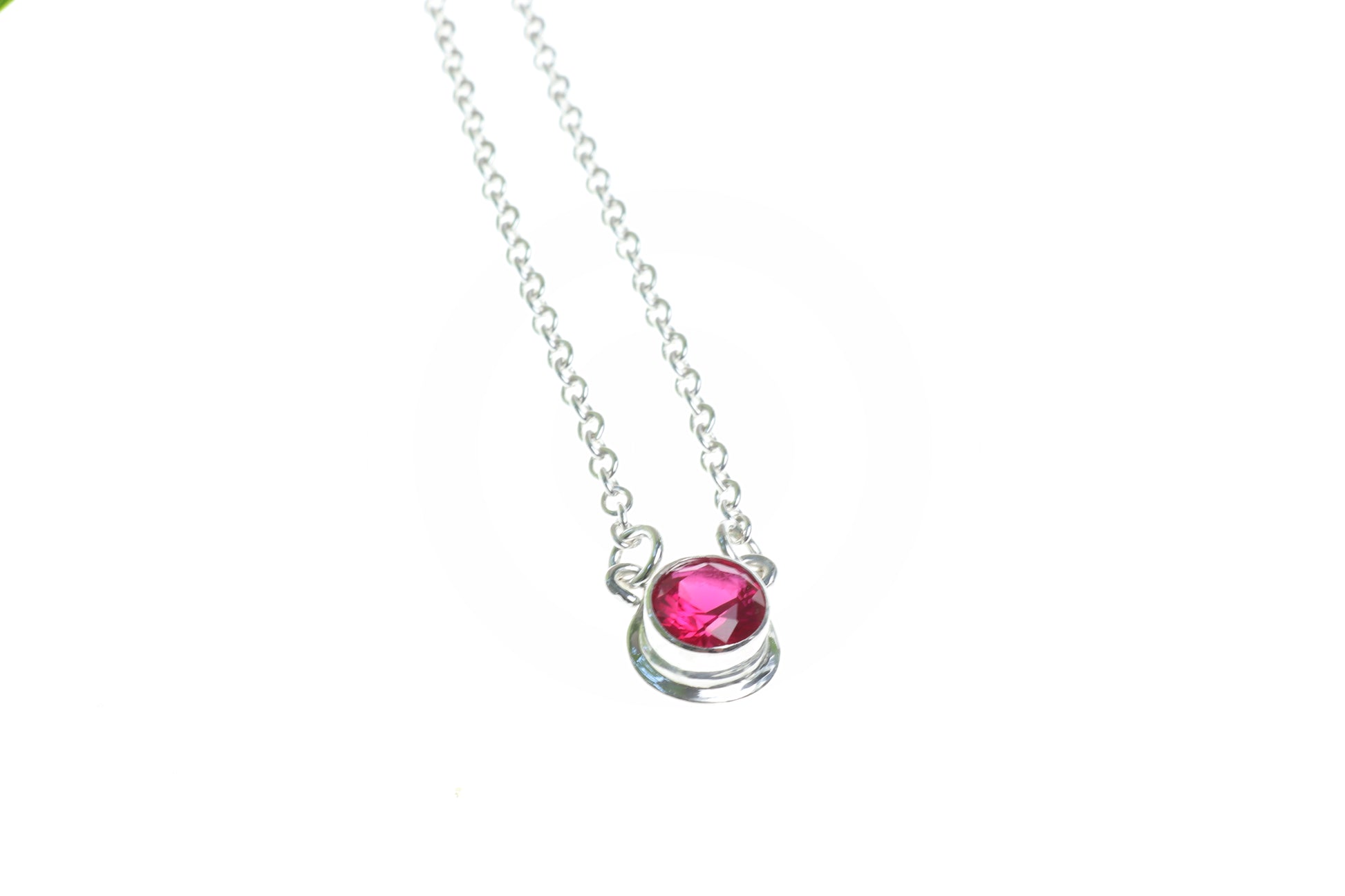 Closeup of ruby 6mm pendant necklace on white background.