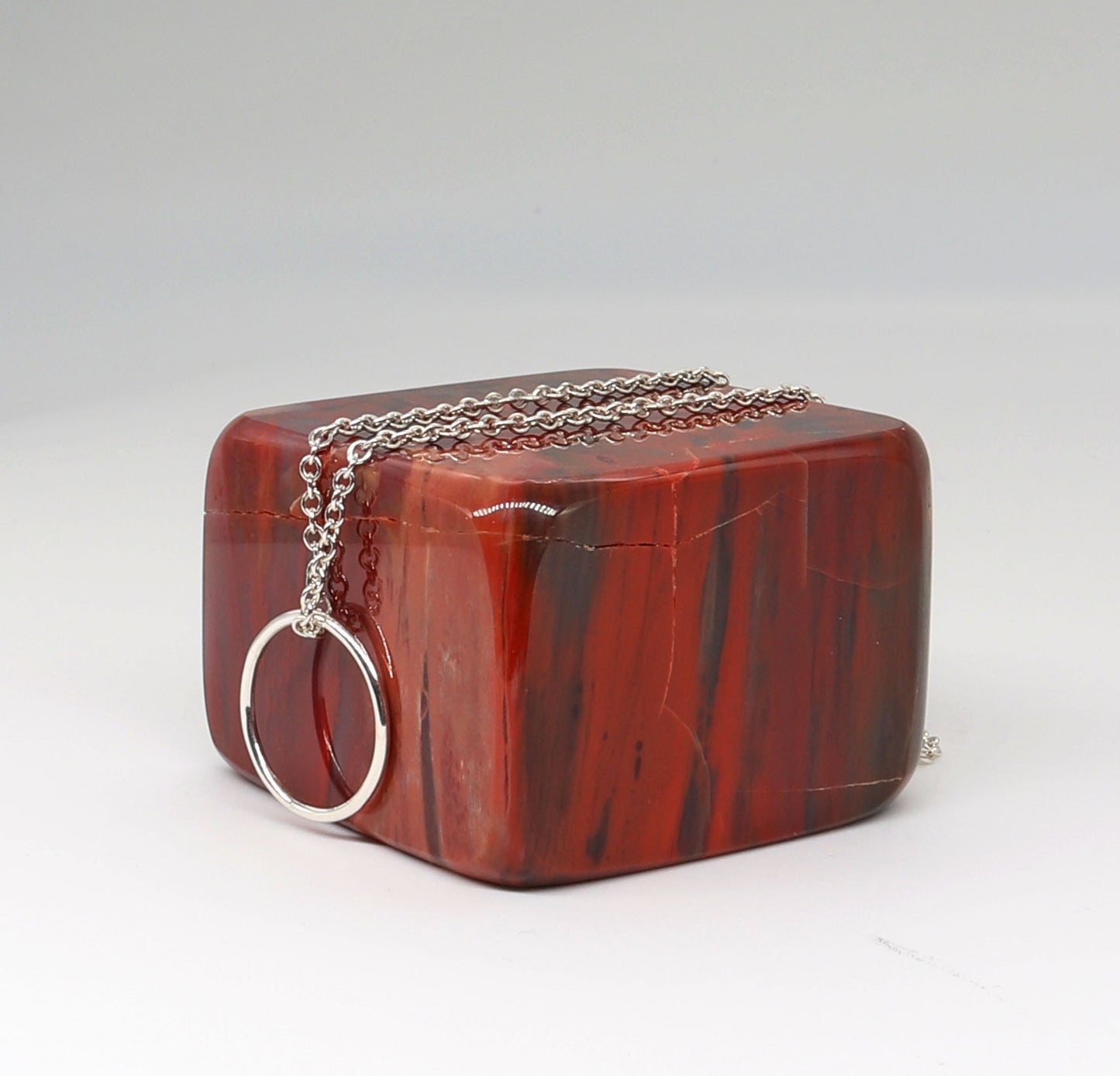 A side view of a handcrafted Open Circle Necklace shown on square block of petrified wood against light gray background, in Argentium® 935 silver.