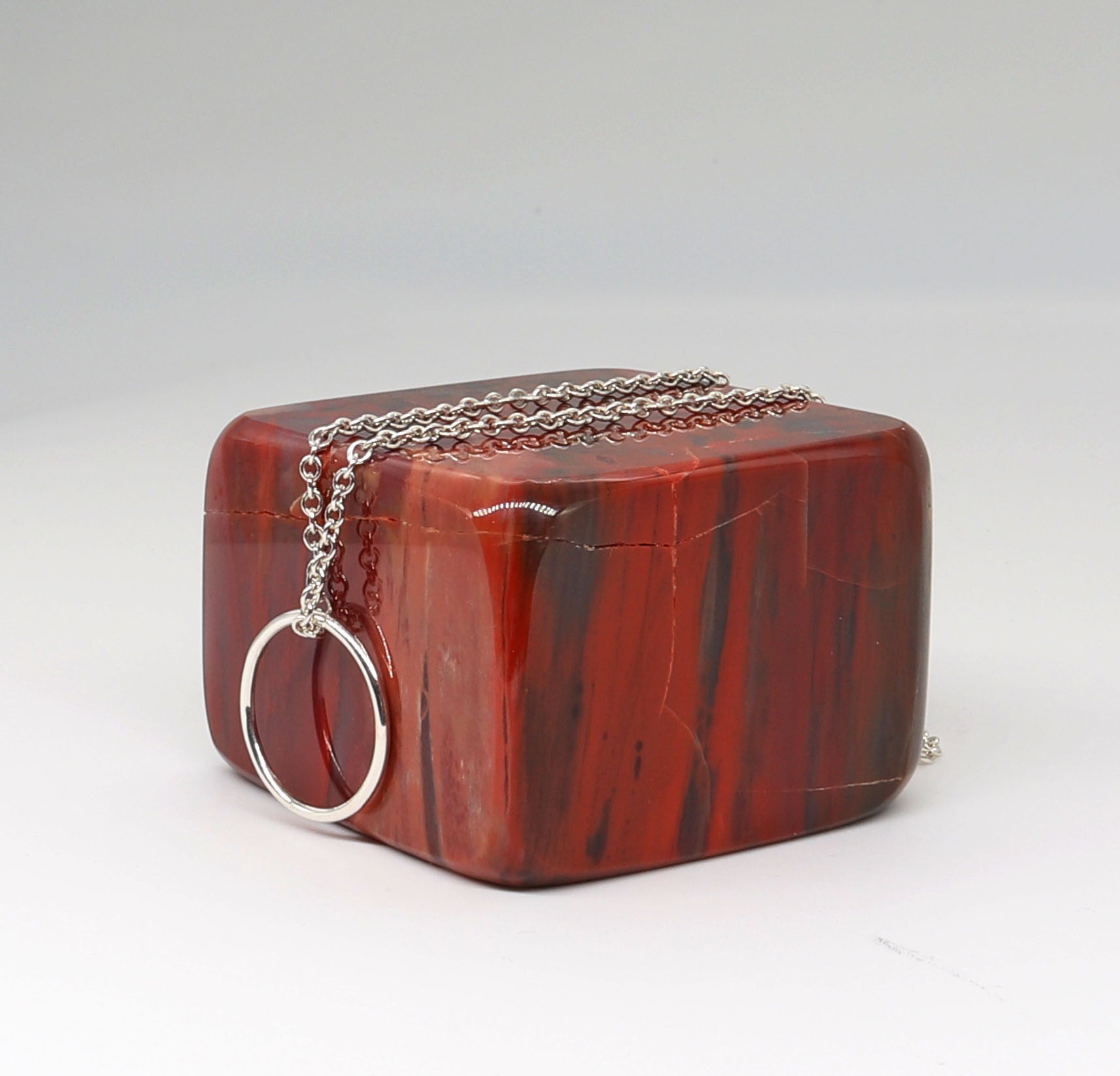 A side view of a handcrafted Open Circle Necklace shown on square block of petrified wood against light gray background, in Argentium® 935 silver.