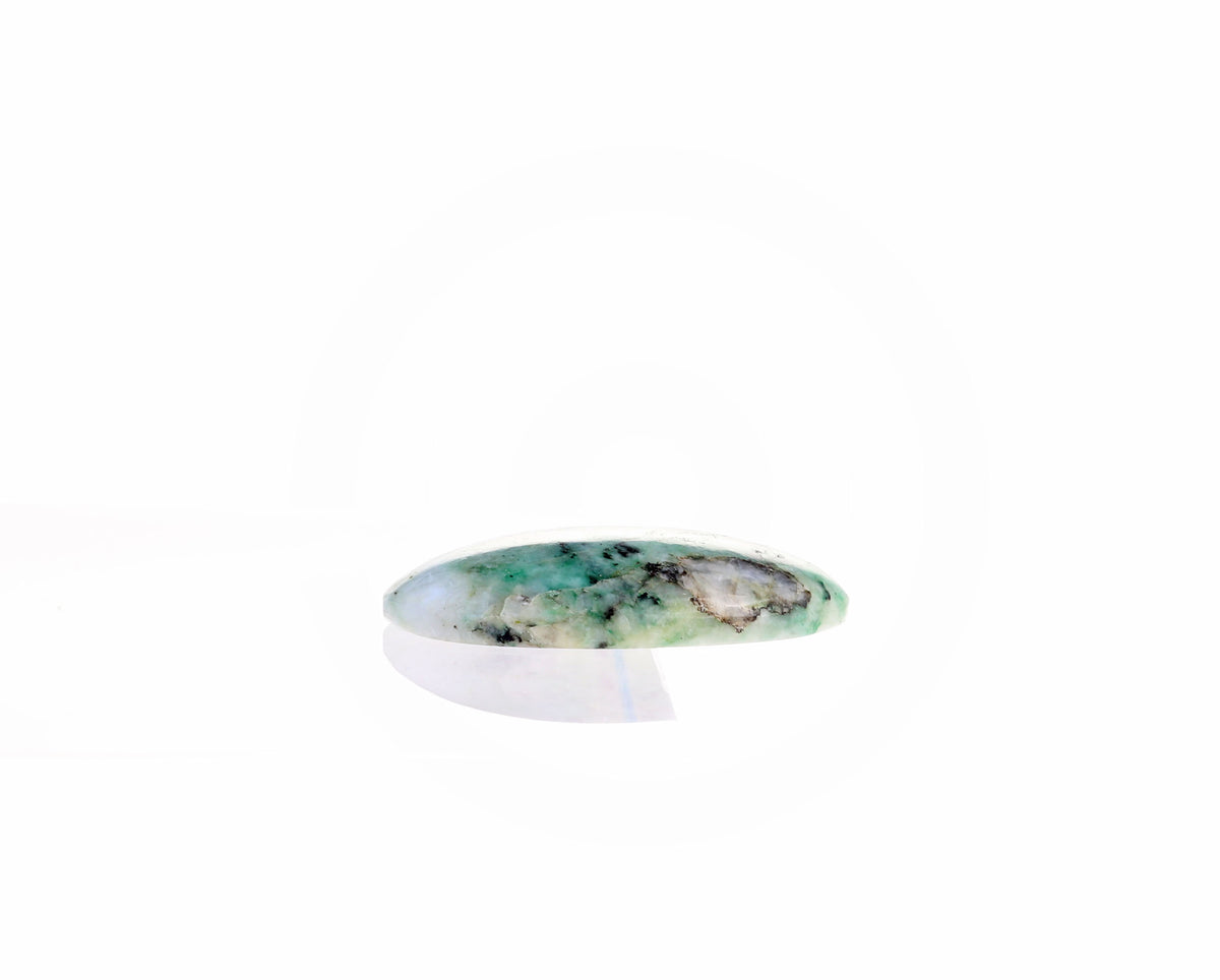 A side view of a hand-cut African Turquoise Jasper cabochon leaning against white marble slab showing its polished dome and 6.22 mm depth.  Shown on white background next to white marble slab., displayed on a clean white background with a soft reflection underneath.