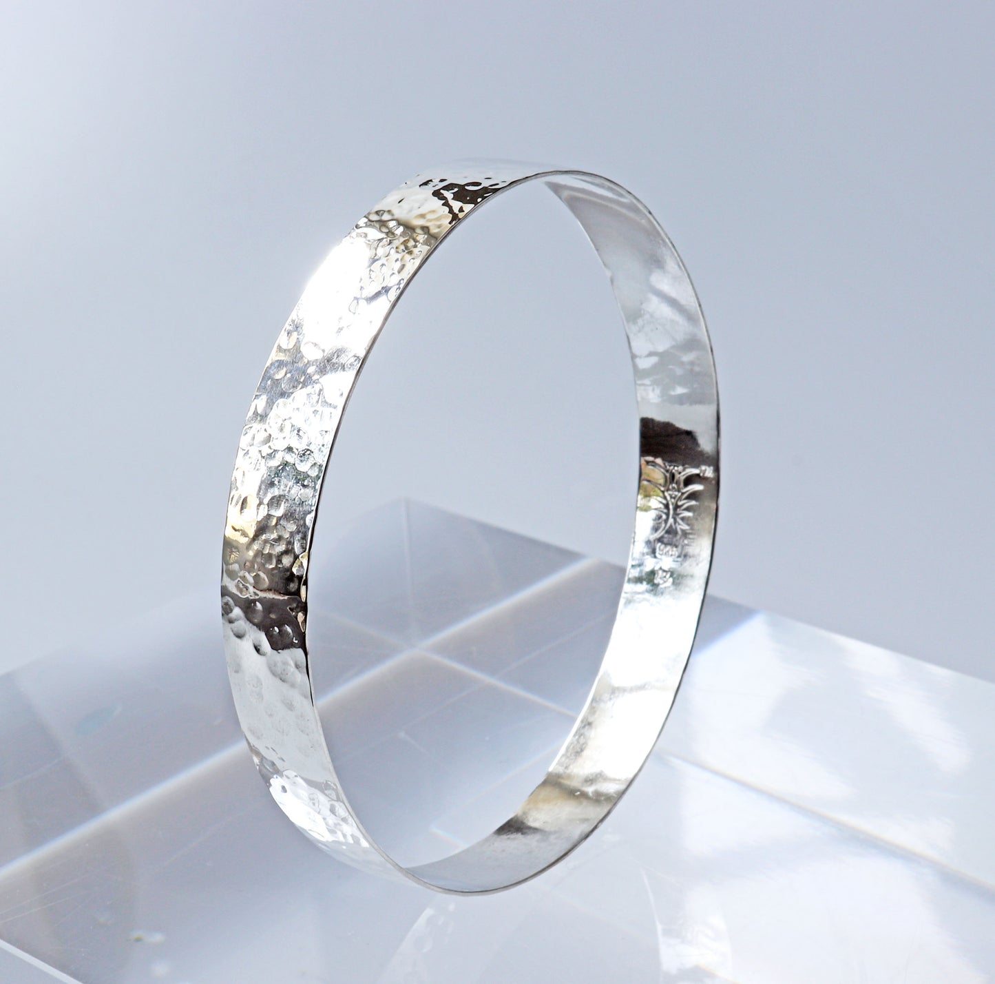 Wide band bangle with faceted hammered texture shown on light gray background.