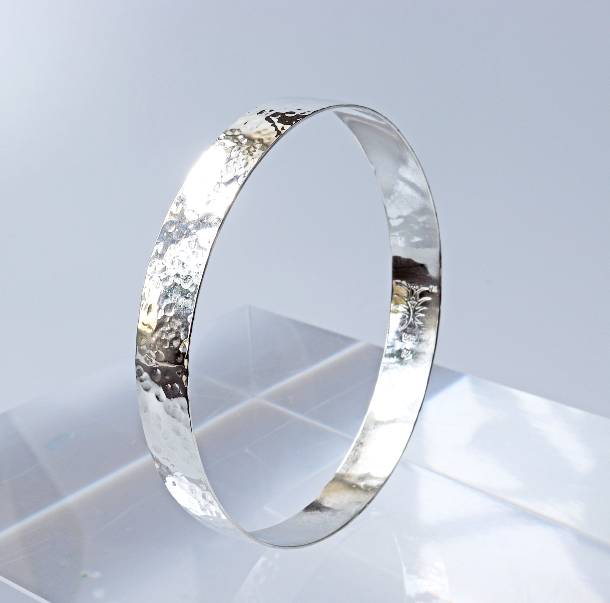Wide band bangle with faceted hammered texture shown on light gray background.