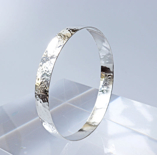 Wide band bangle with faceted hammered texture shown on light gray background.