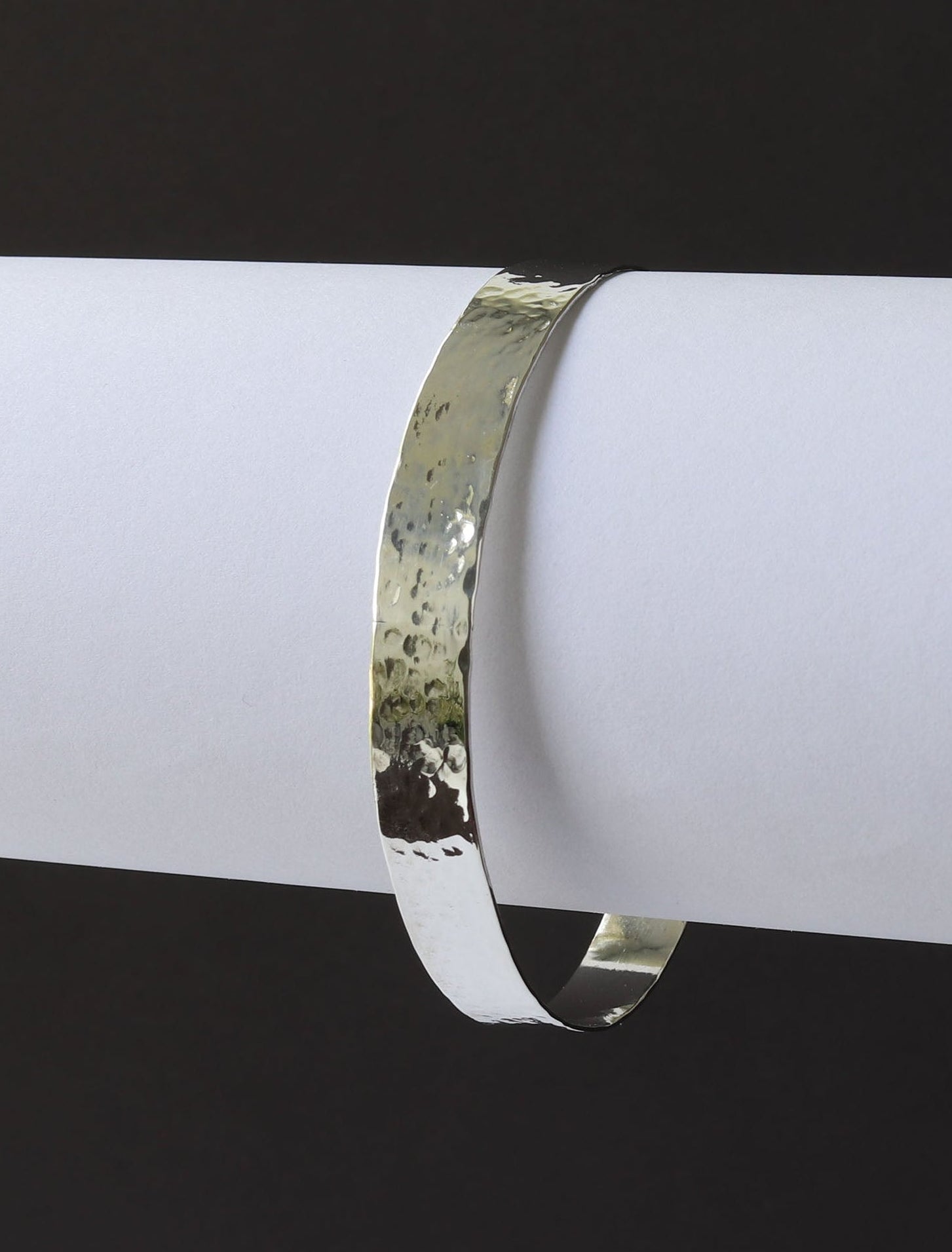 Argentium Silver Bangle with hammered features against white and black background.