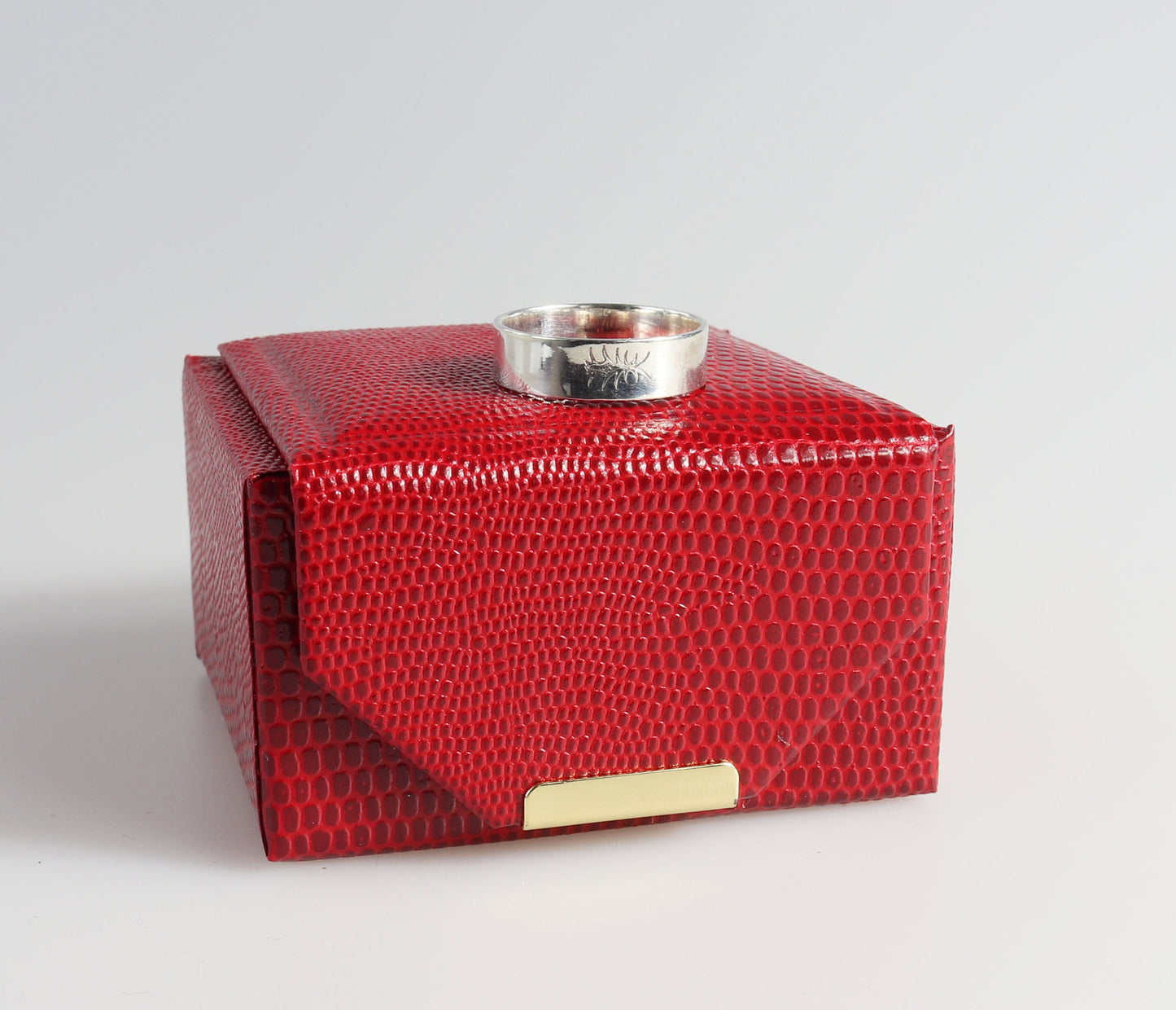 Red textured jewelry box with a silver ring on a light gray background