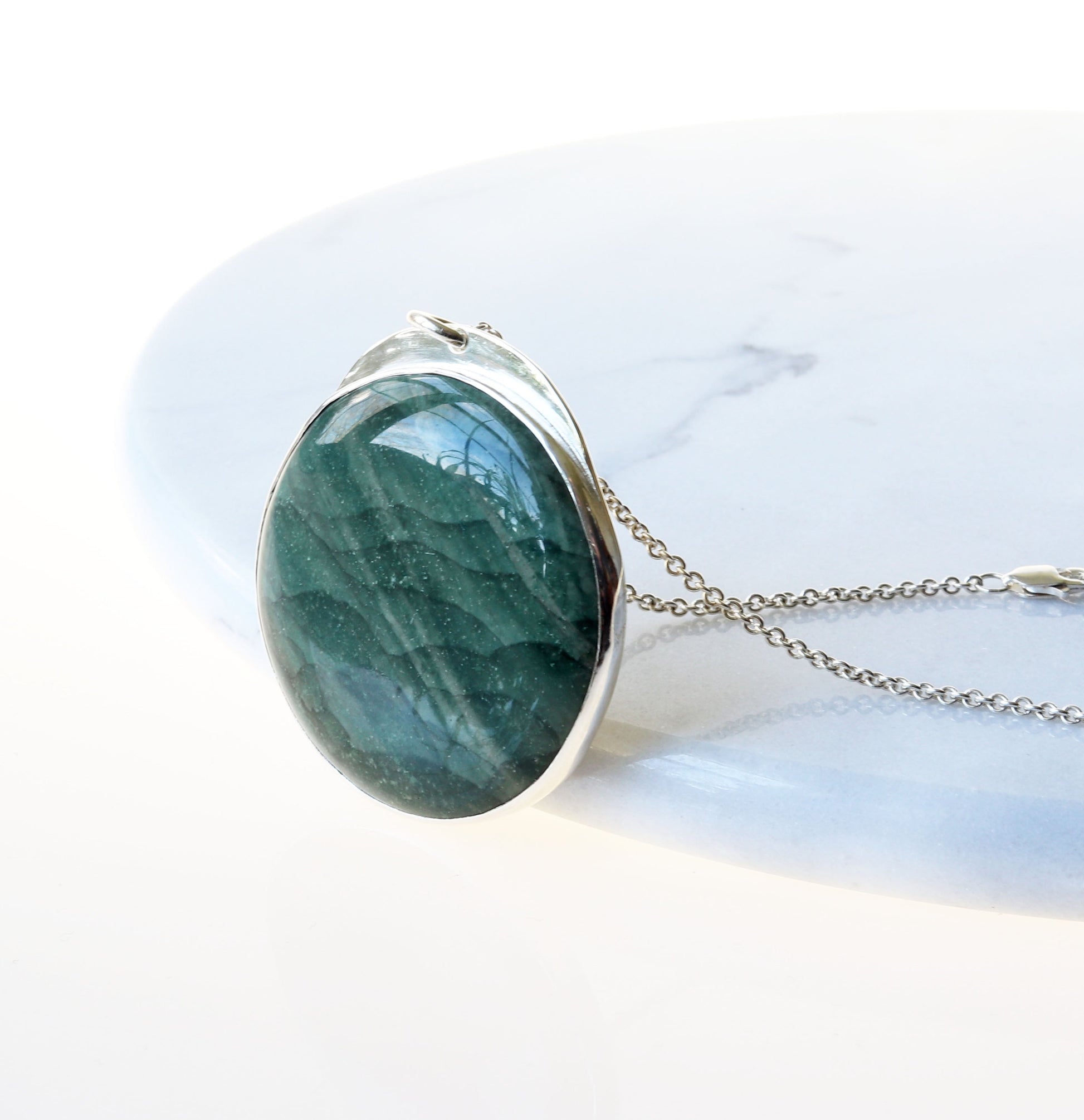 Angle view of Arizona Lizard Pendant set in Argentium Silver shown against white marble slab.