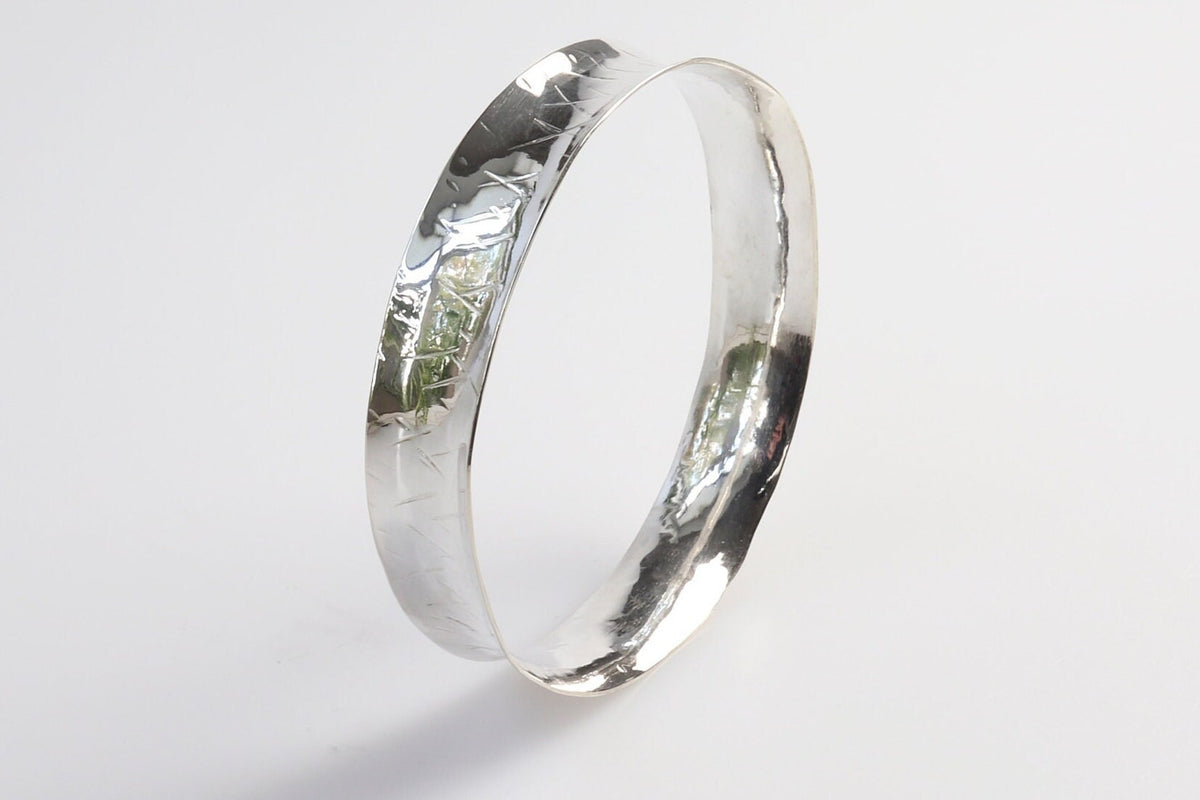 Solid Argentium 935 silver bangle with herringbone-style texture and gently flared edges, standing upright on a light background.