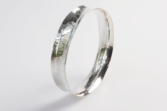 Solid Argentium 935 silver bangle with herringbone-style texture and gently flared edges, standing upright on a light background.