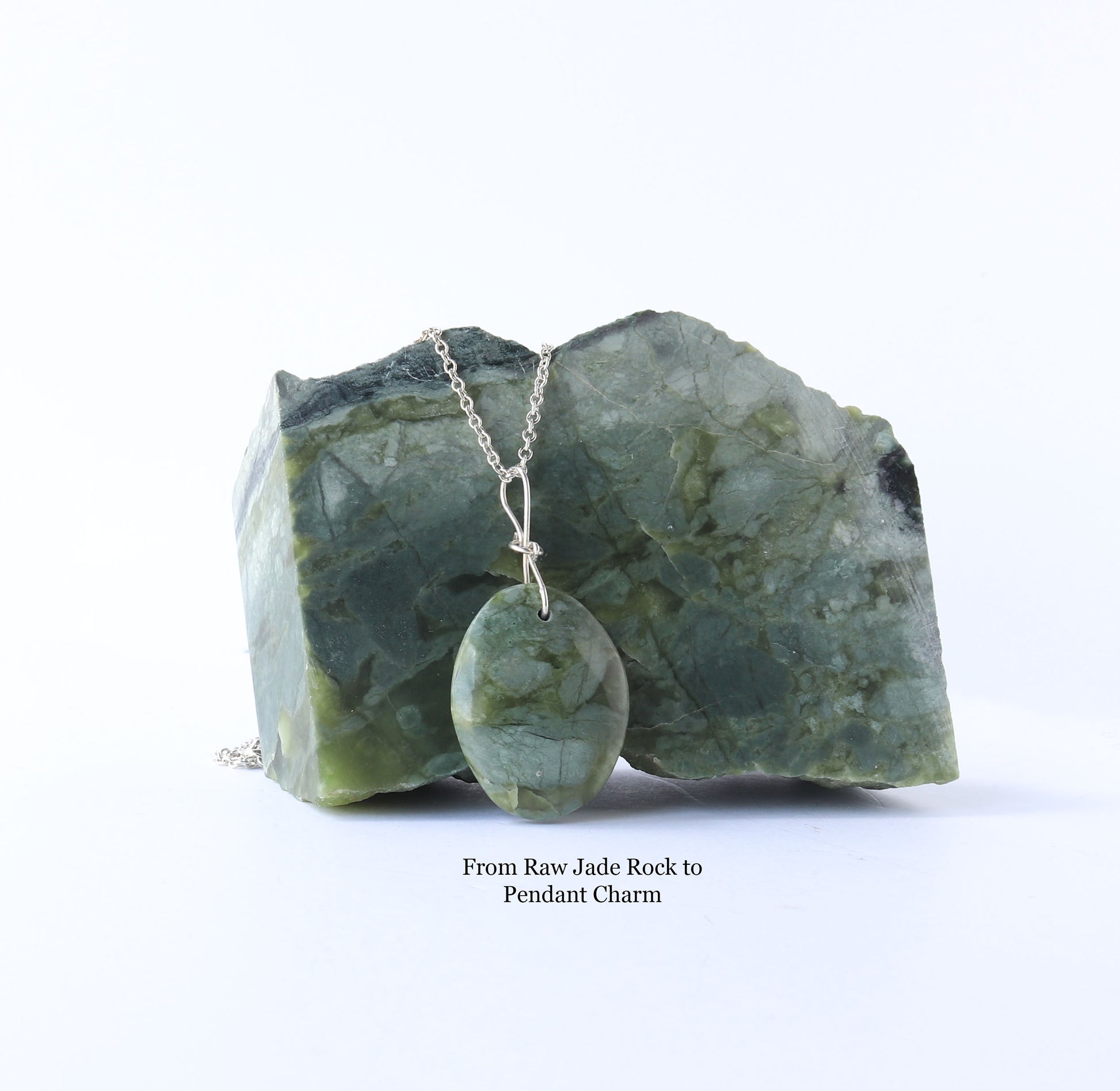 A polished California jade oval pendant charm suspended from a silver chain and displayed on top of the raw jade rock  against a white background. Text below reads 'From Raw Jade Rock to Pendant Charm'.